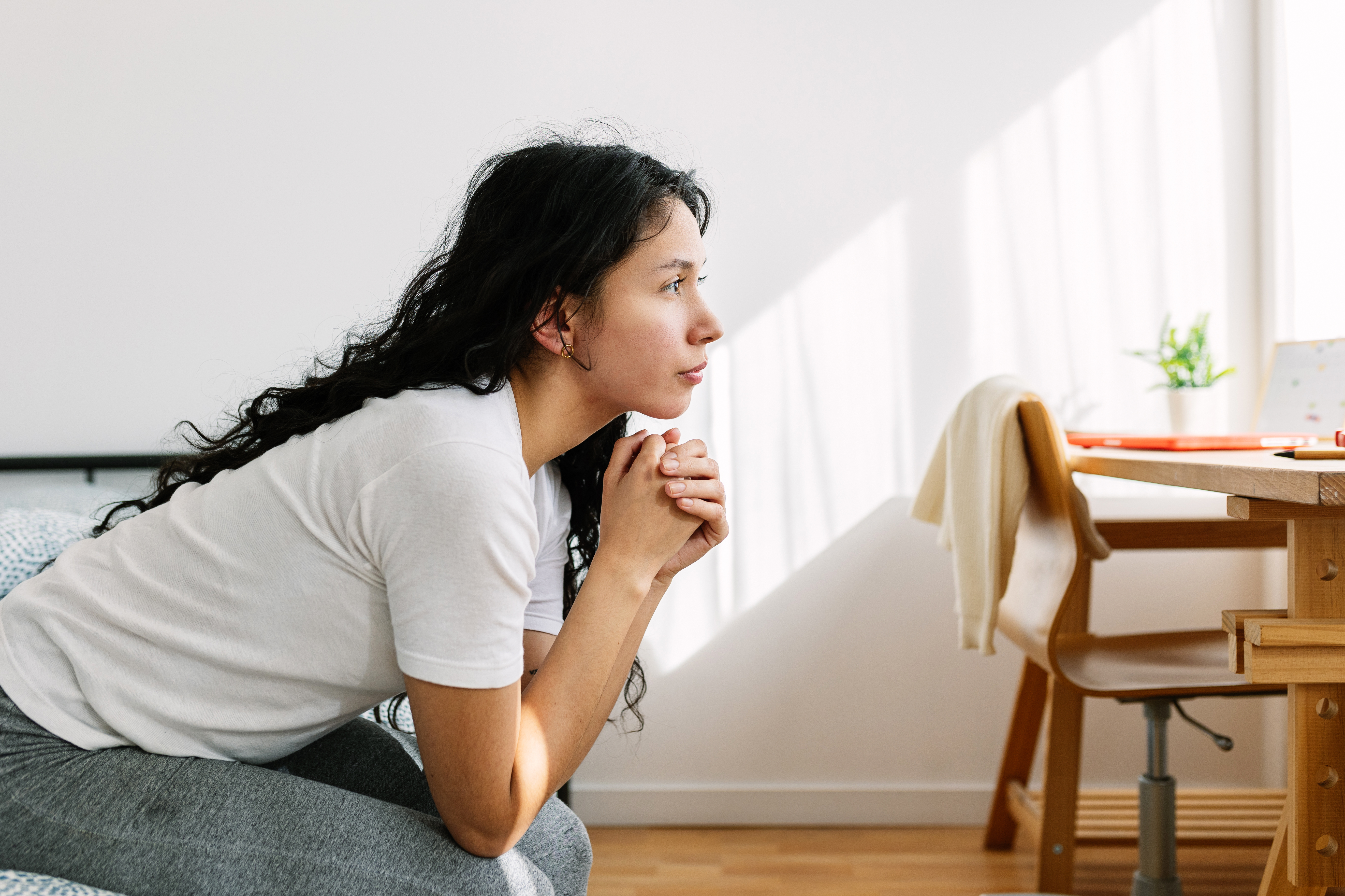 Sad and lonely thoughtful teenage girl looking away sitting on bed in the room. Social issue and adolescence bullying concept | Source: Getty Images