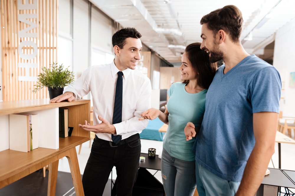 A salesman at a furniture store showing some pieces to an interested couple. | Photo: Shutterstock