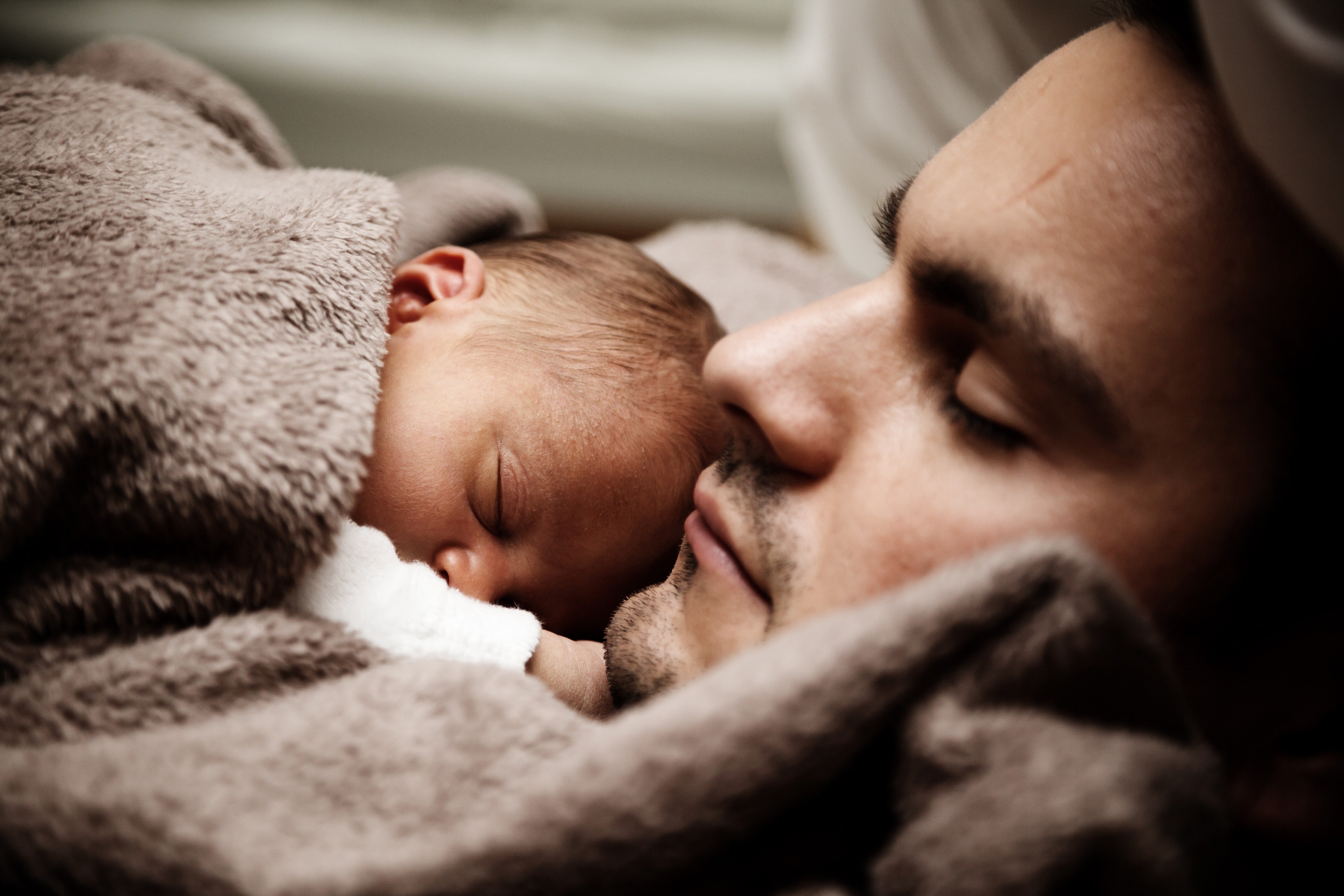 Un hombre recostado en una cama con un bebé. | Foto: Pexels