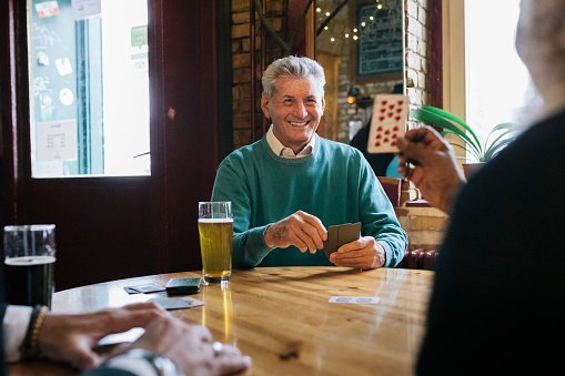 Photo of a mature man smiling and enjoying a card game with his friends at their local bar. | Photo: Getty Images