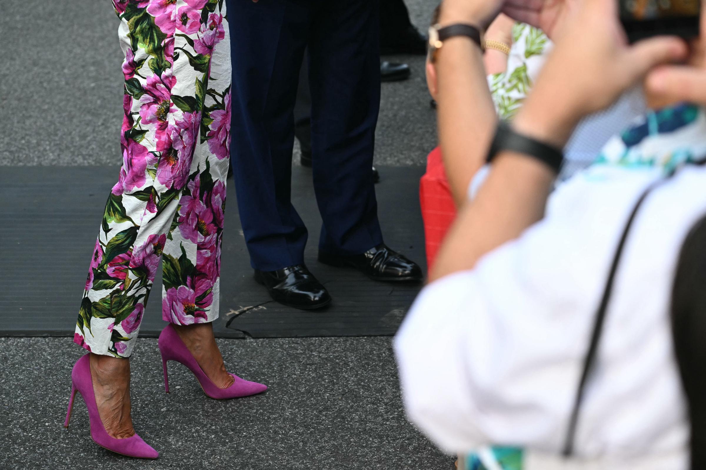 A close-up of Melania and Donald Trump's shoes captures a stylish detail from the event. Melania sports bright fuchsia heels with floral trousers, while Donald wears polished black dress shoes, adding flair and contrast to the gathering.