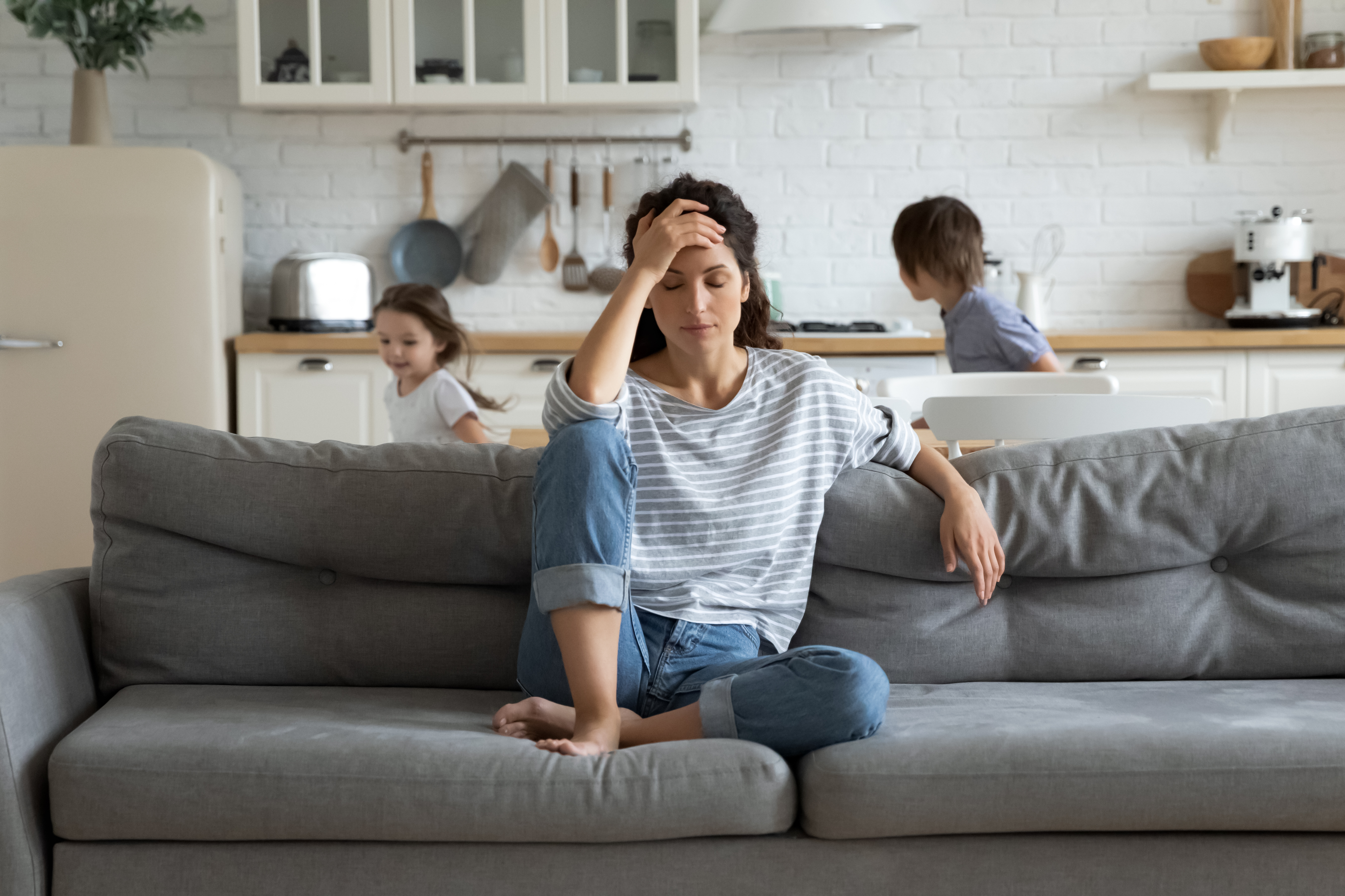 A woman sitting on the couch and looking problematic as two kids run around behind her | Source: Shutterstock