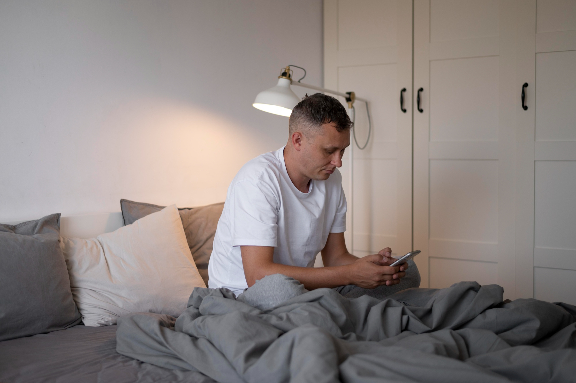 A man looking at a phone while covered in a sheet in bed | Source: Freepik