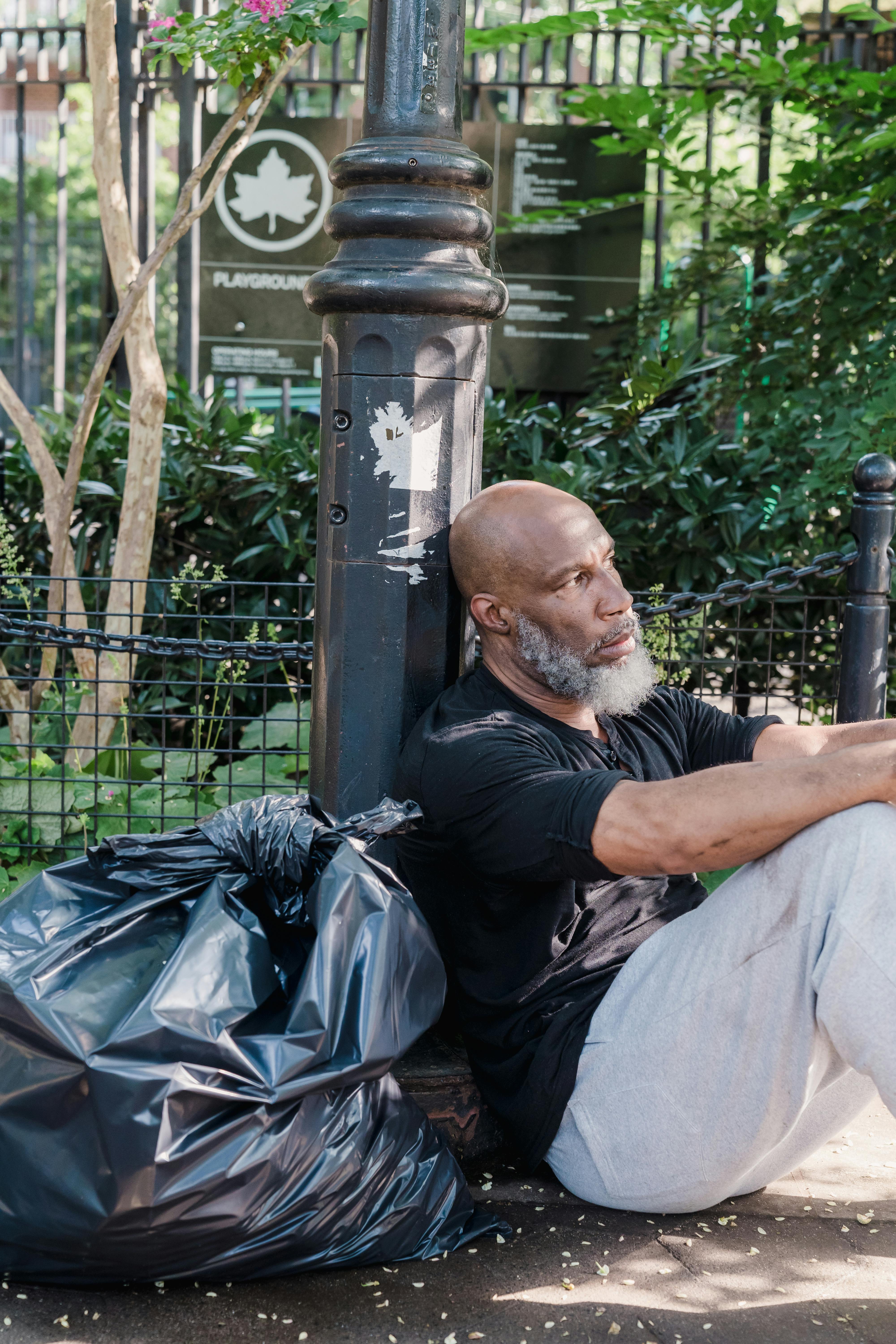 A homeless man sitting near metal post | Source: Pexels