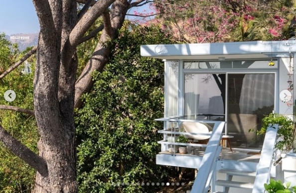 Seen from the grounds, part of the residence appears tucked among mature trees and thick greenery, with a compact terrace extending from its glass facade. The Hollywood sign is visible in the distance, offering a reminder of the property's location in the Los Feliz hills above Los Angeles. | Source: Instagram/jparkerstanton