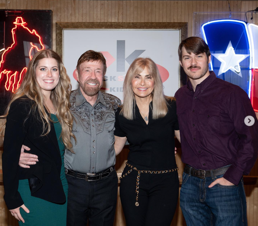 Chuck Norris stands arm-in-arm with Gena O'Kelley Norris, Danilee Norris, and Dakota Norris, the group smiling warmly in a close-knit family moment framed by rustic décor and glowing neon lights. | Source: Instagram/chucknorris