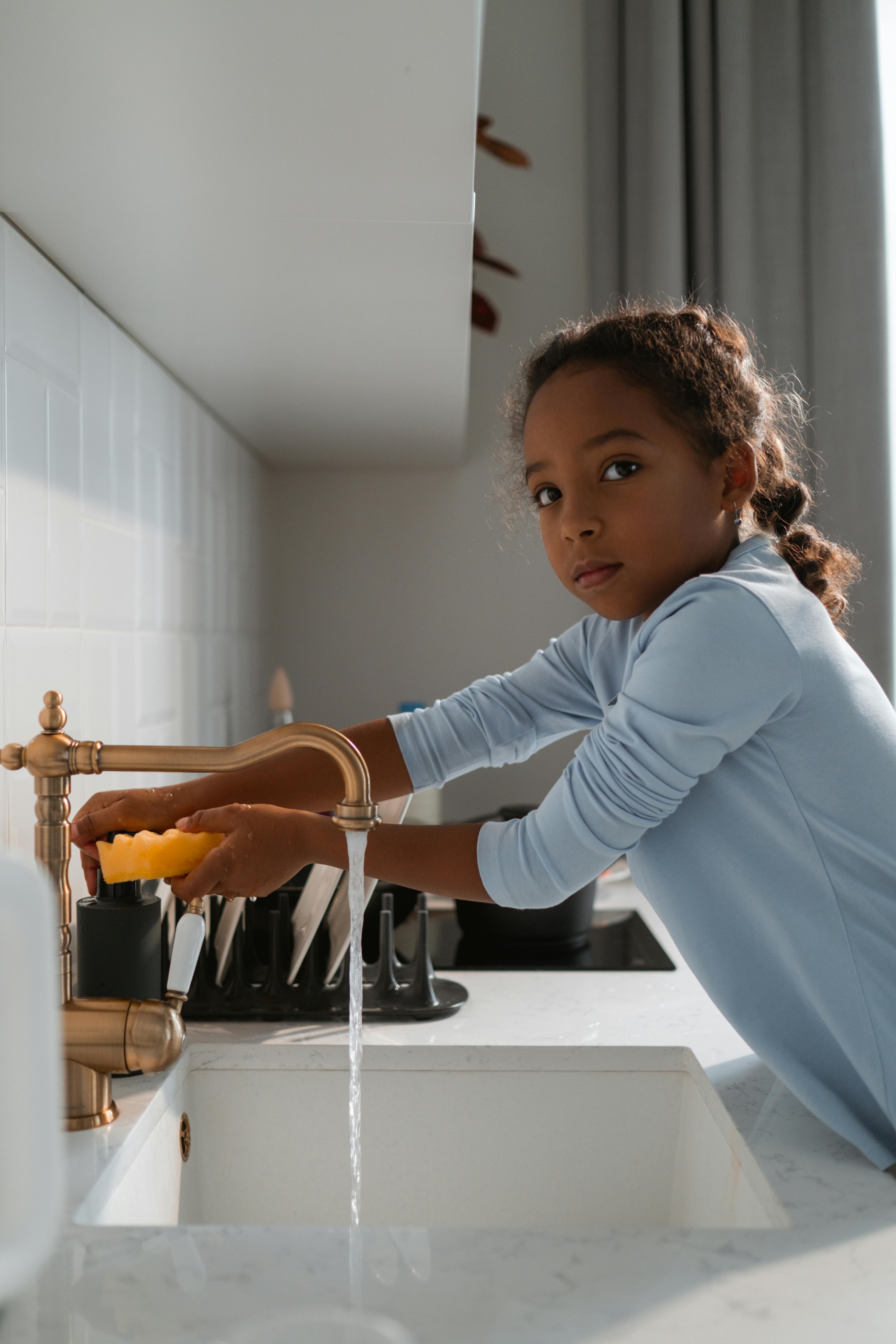 A little girl running water at the kitchen sink | Source: Pexels