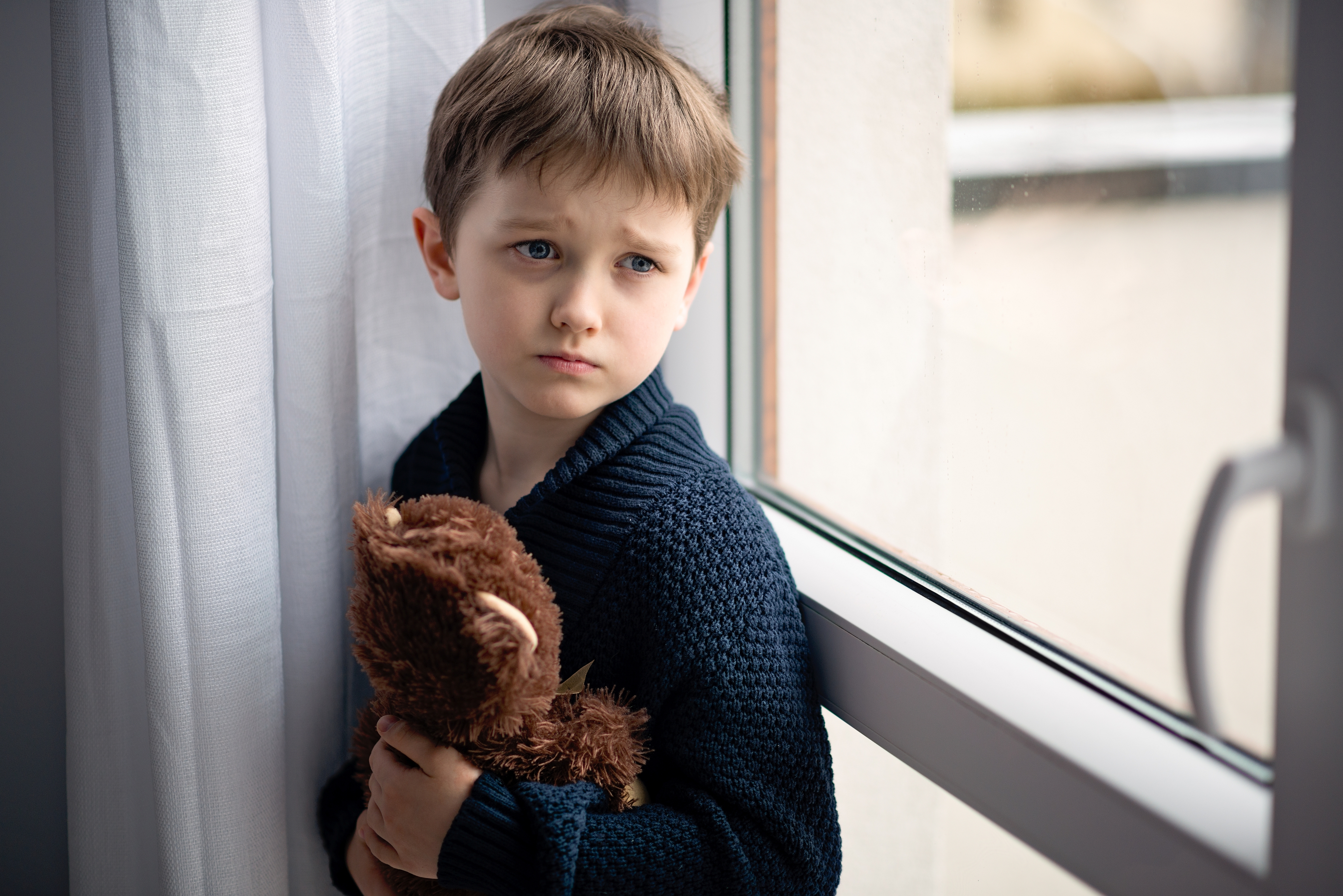 A sad young boy holding a teddy bear | Source: Shutterstock