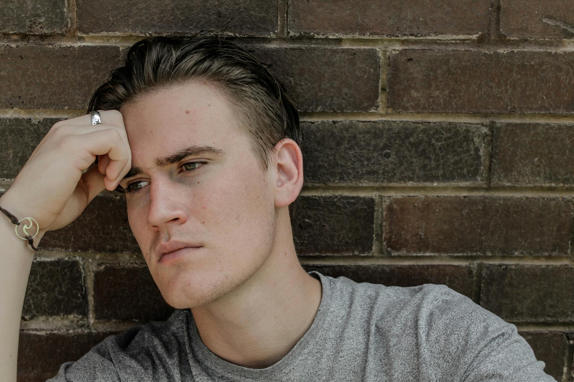 A distressed man lost in his thoughts while sitting against a brick wall | Source: Pexels