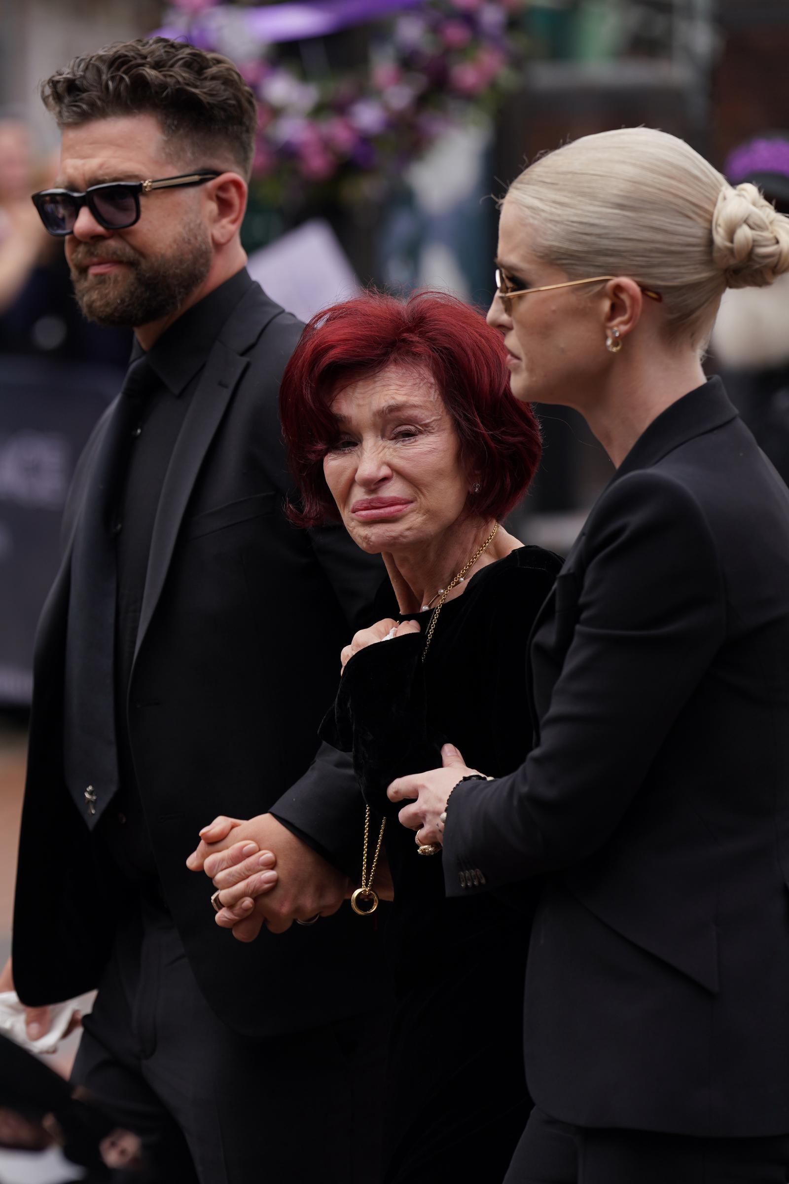 Jack and Kelly Osbourne share in their mother's grief as they attend the late Ozzy's funeral procession. Their mother Sharon is visibly heartbroken as she view the messages and floral tributes left at the Black Sabbath Bridge.