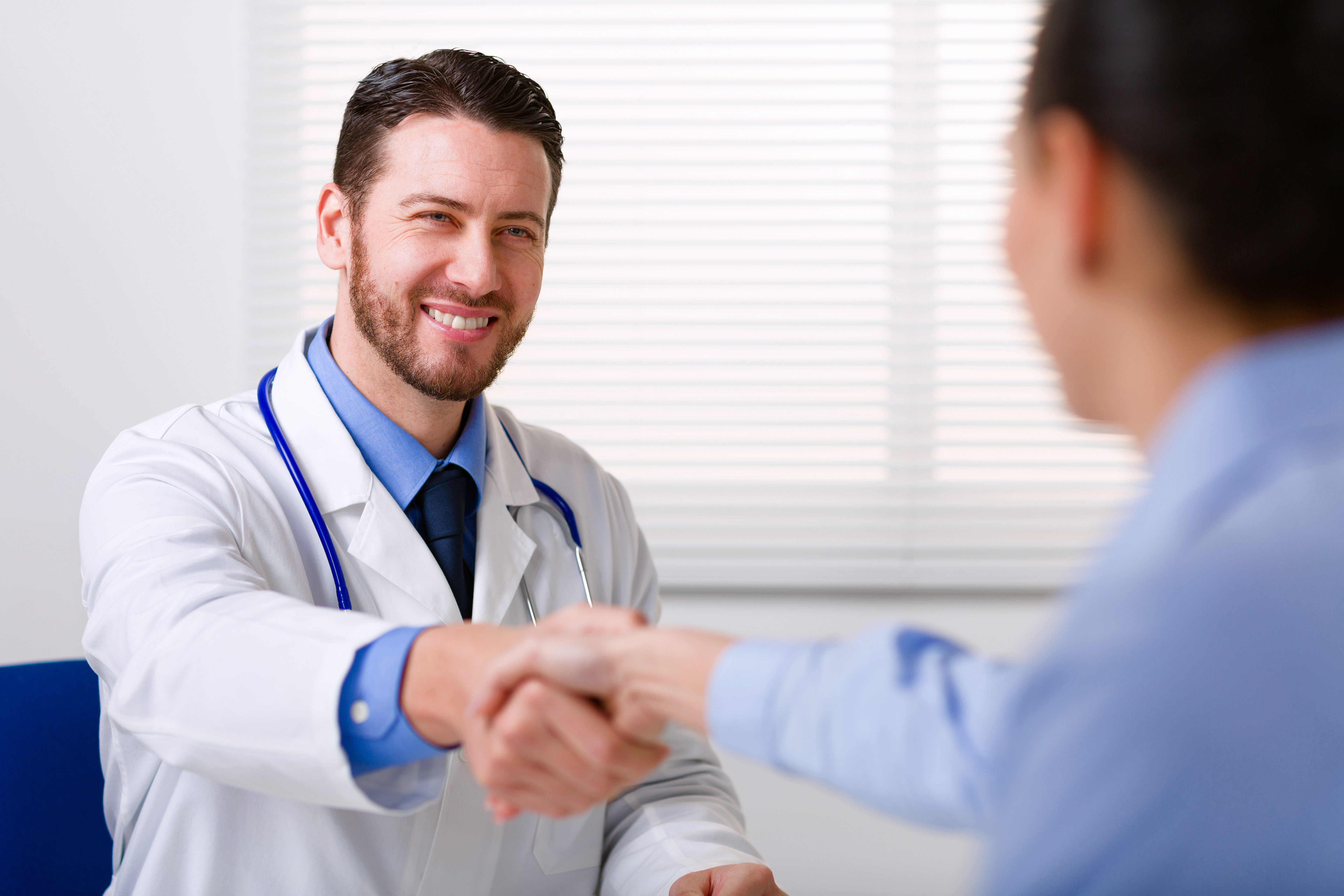 Male doctor in white coat smiling while shaking hand to woman. | Source: Shutterstock
