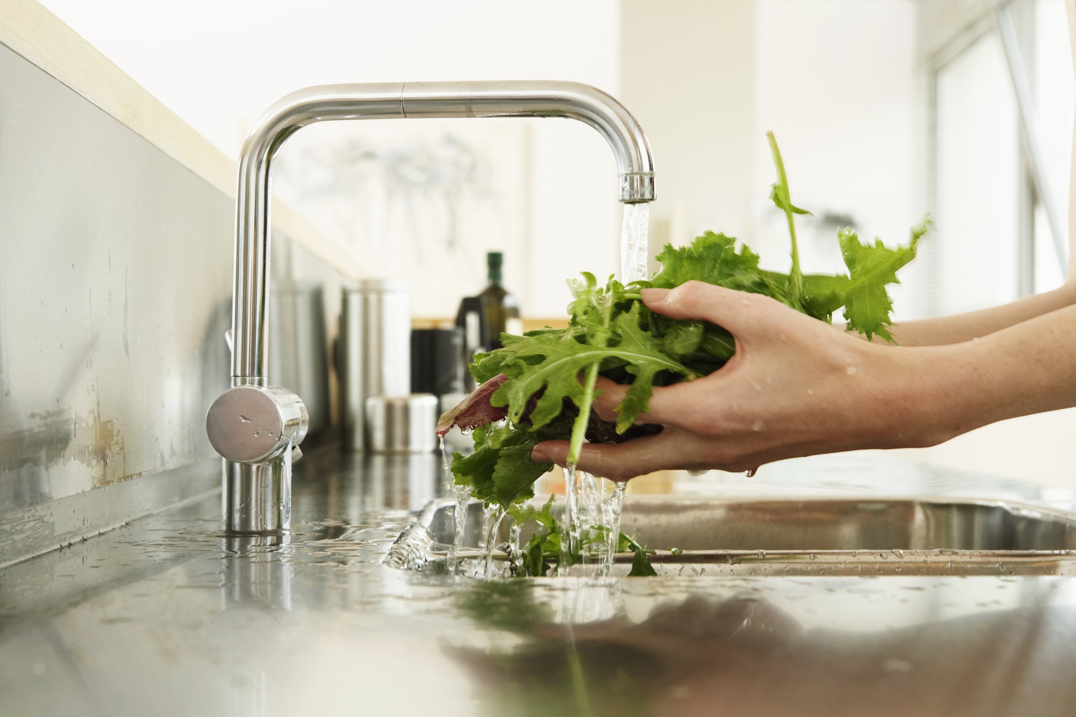 Une femme lavant de la laitue à l'évier de la cuisine. | Photo : Getty Images