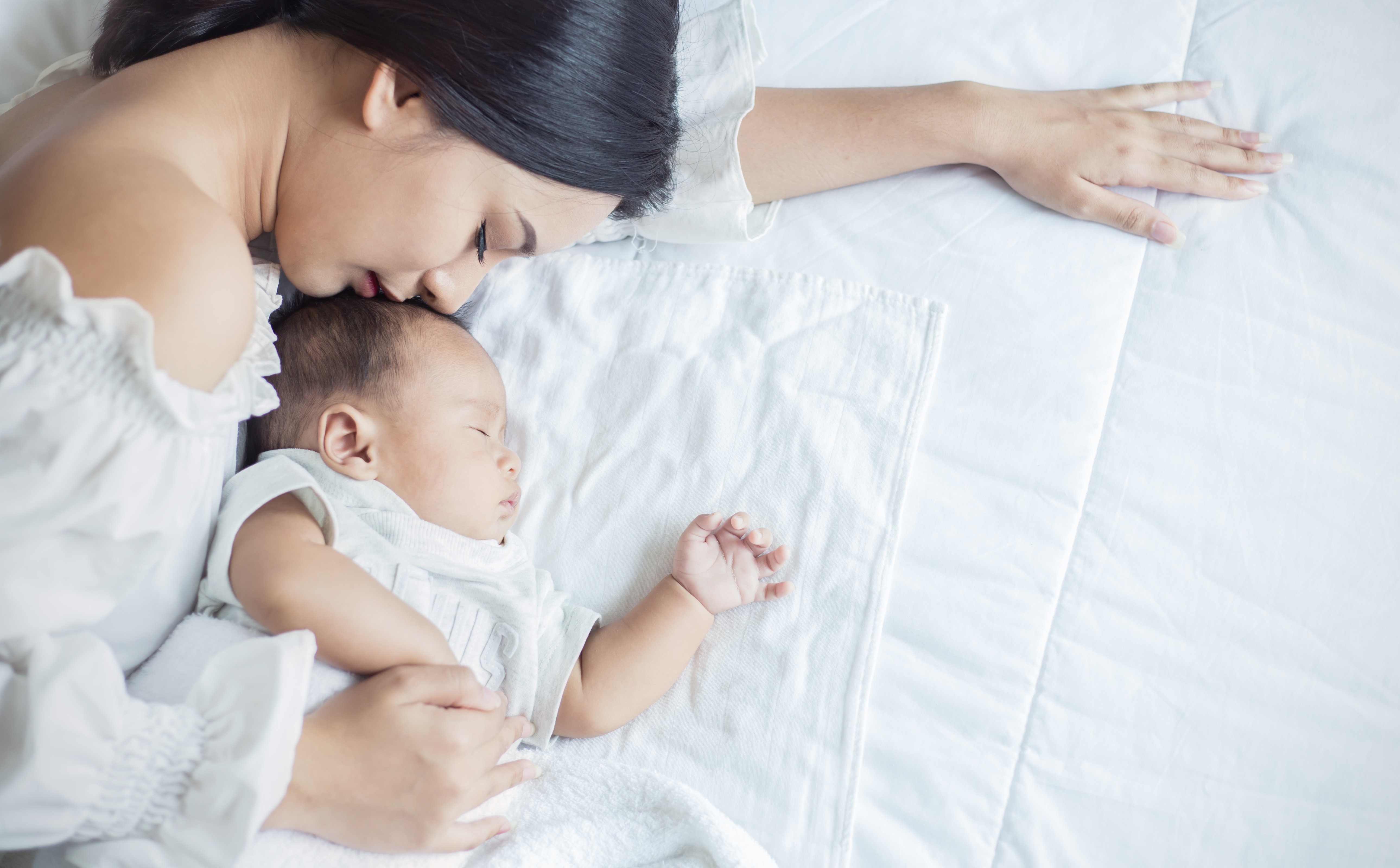 Porträt einer Mutter, die ihr gesundes Neugeborenes küsst, das im Bett schläft | Quelle: Shutterstock