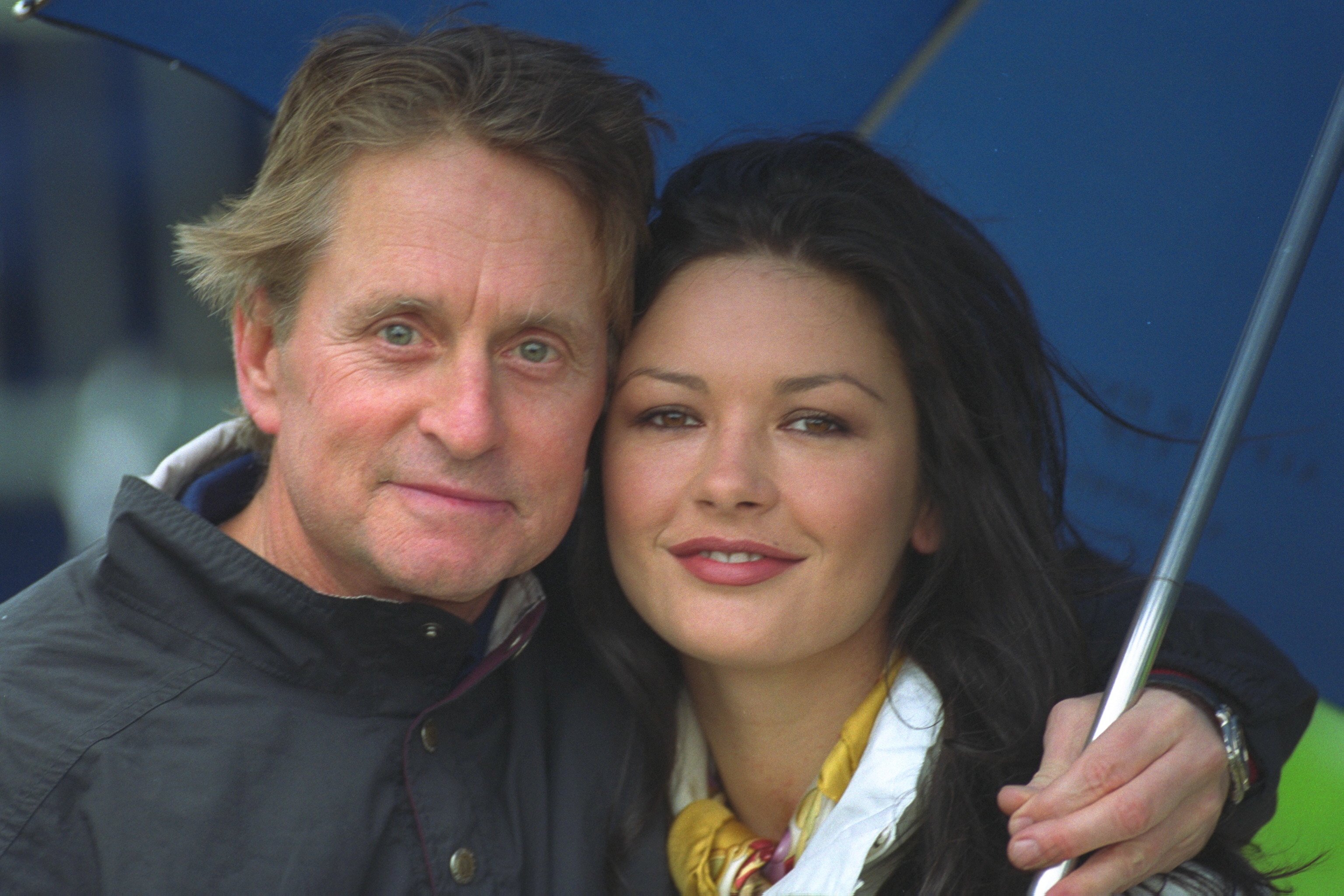 Michael Douglas and Catherine Zeta-Jones shelter from the drizzle while playing golf at St. Andrews on October 11, 2000 ┃Source: Getty Images