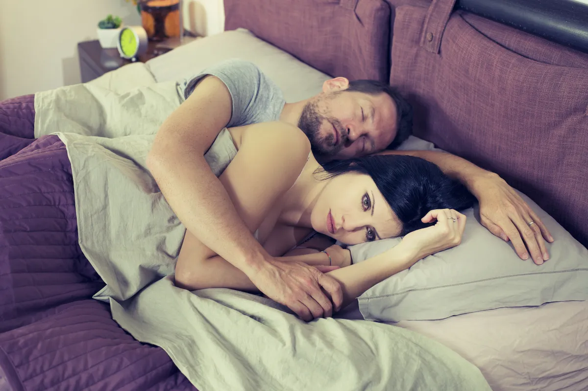 Eine Frau sieht besorgt aus, während ihr Mann neben ihr schläft. | Source: Shutterstock
