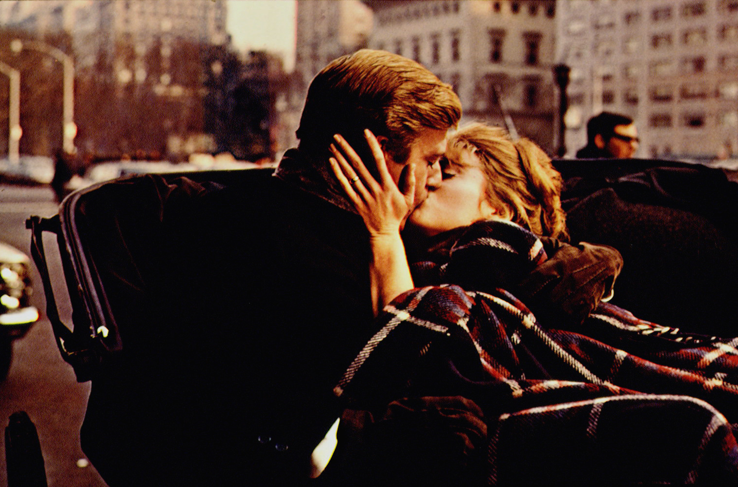 Robert Redford and Jane Fonda on the set of "Barefoot in the Park," directed by Gene Saks, share a passionate kiss beside their car as Fonda gently holds Redford's face in the romantic scene.