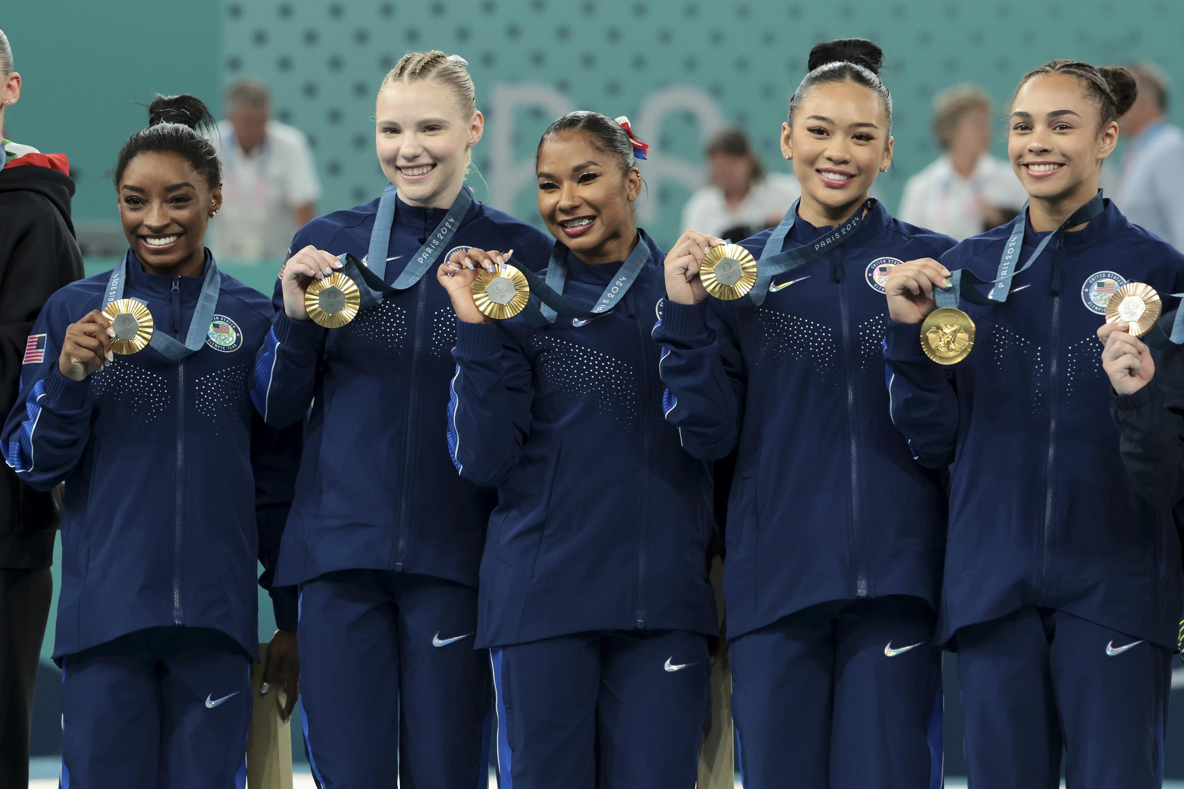 Gold medalists Simone Biles, Jade Carey, Jordan Chiles, Sunisa Lee, and Hezly Rivera celebrate on the podium during the Artistic Gymnastics Women's Team Final at the Paris 2024 Olympics in Paris, France on July 30, 2024 | Source: Getty Images