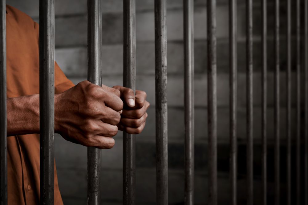 Man in orange tightly holding prison bars. | Source: Shutterstock 