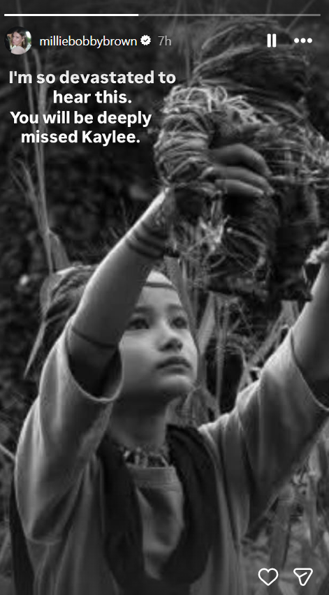 A black-and-white image from "Godzilla vs. Kong" shows Kaylee Hottle as Jia lifting a bundle of vegetation while looking upward. Millie Bobby Brown shared the still on her Instagram Story alongside a message mourning Kaylee after news of the actress's death broke. | Source: Instagram/milliebobbybrown