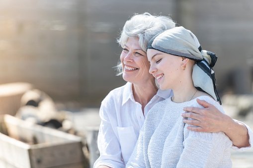 A beautiful young woman with cancer is wearing a head scarf and is embracing her mother. | Photo: Getty Images