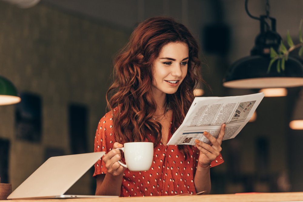 A woman holding a cup of coffee while reading a newspaper | Photo: Shutterstock/LightField Studios