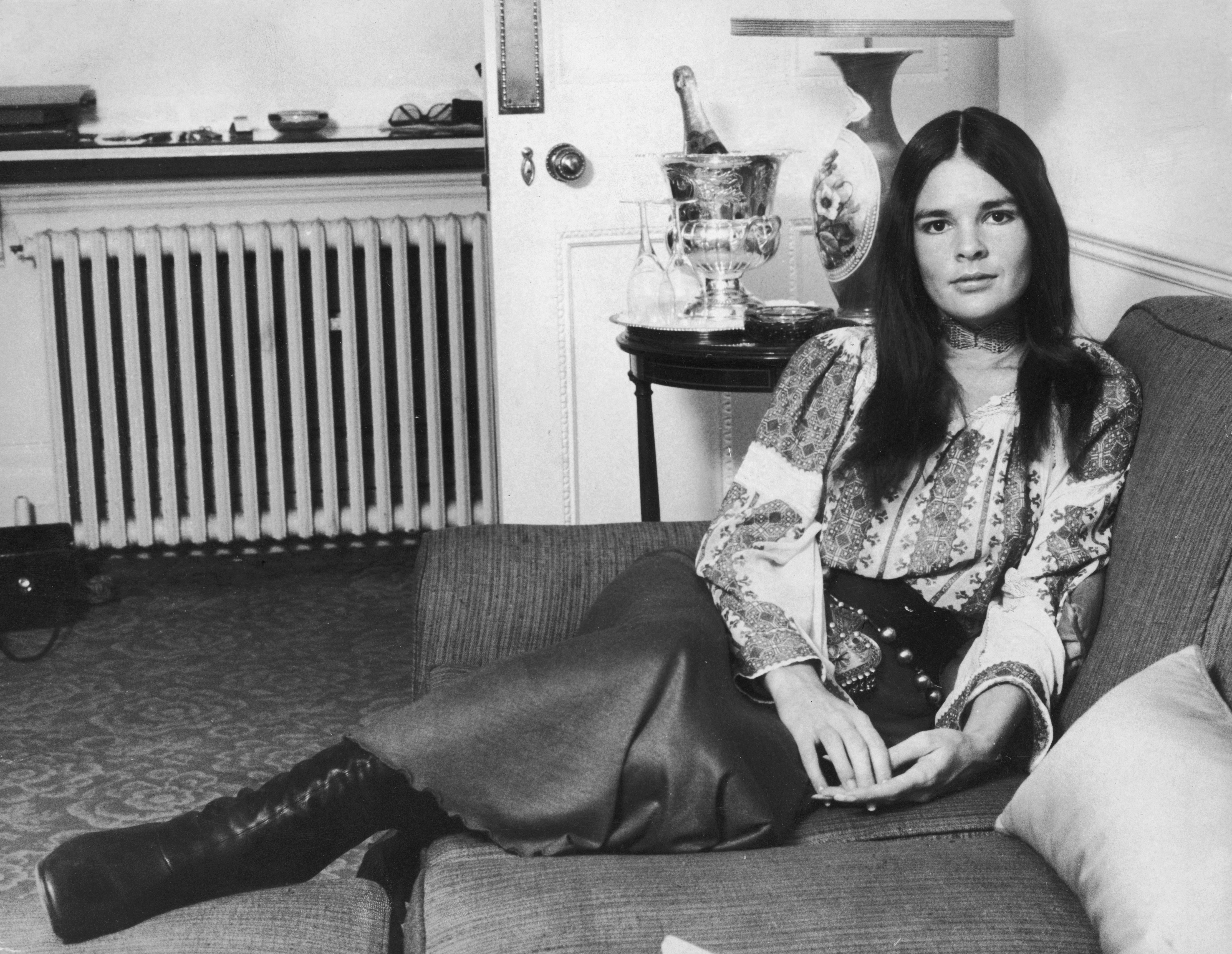 Style icon and former model Ali MacGraw seated on the couch wearing leather boots paired with a long skirt and a floral blouse on March 8, 1971. | Source: Getty Images