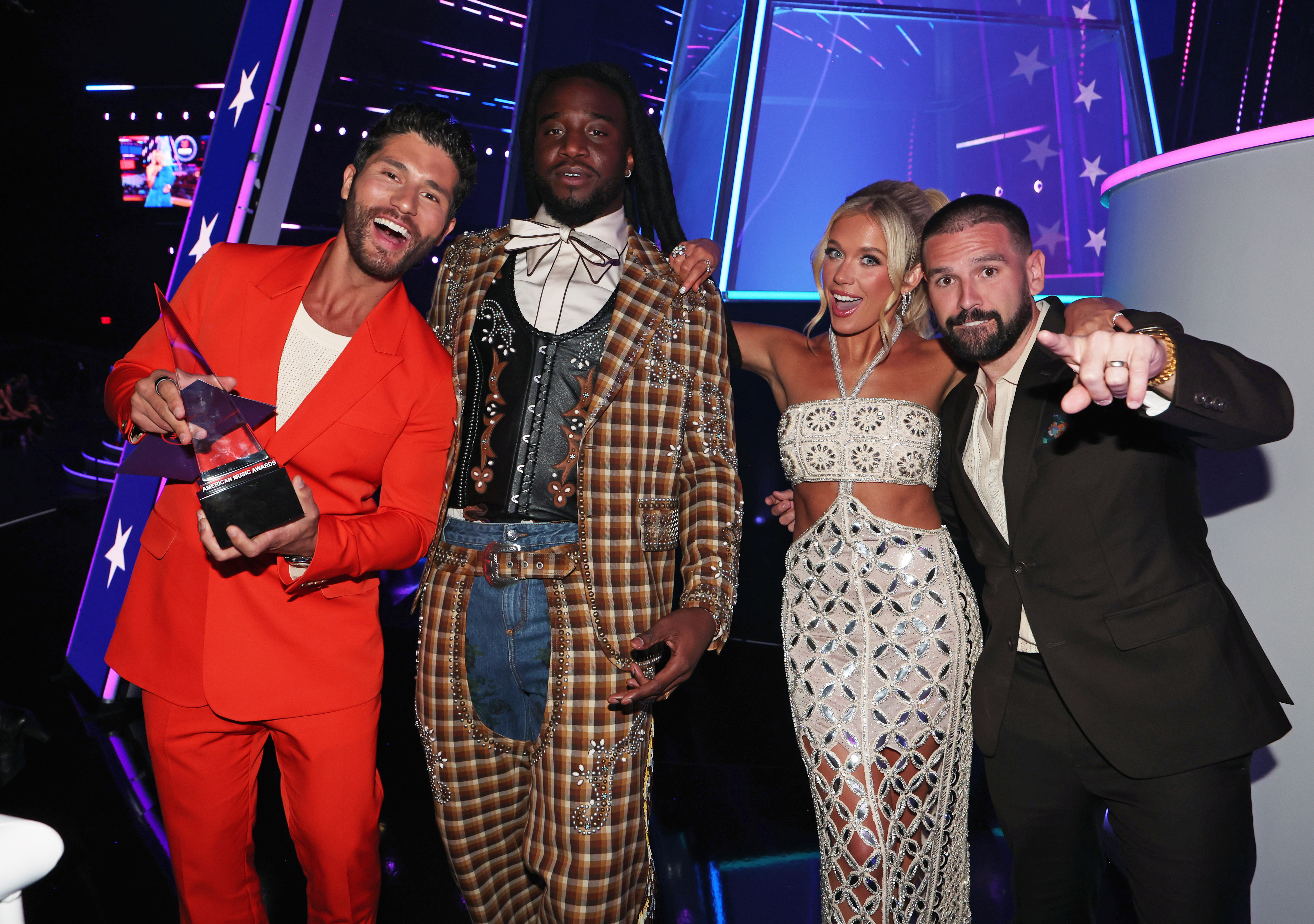 Beaming with excitement, she celebrates backstage with the award-winning crew, soaking in the high-energy moment amid neon-lit surroundings.