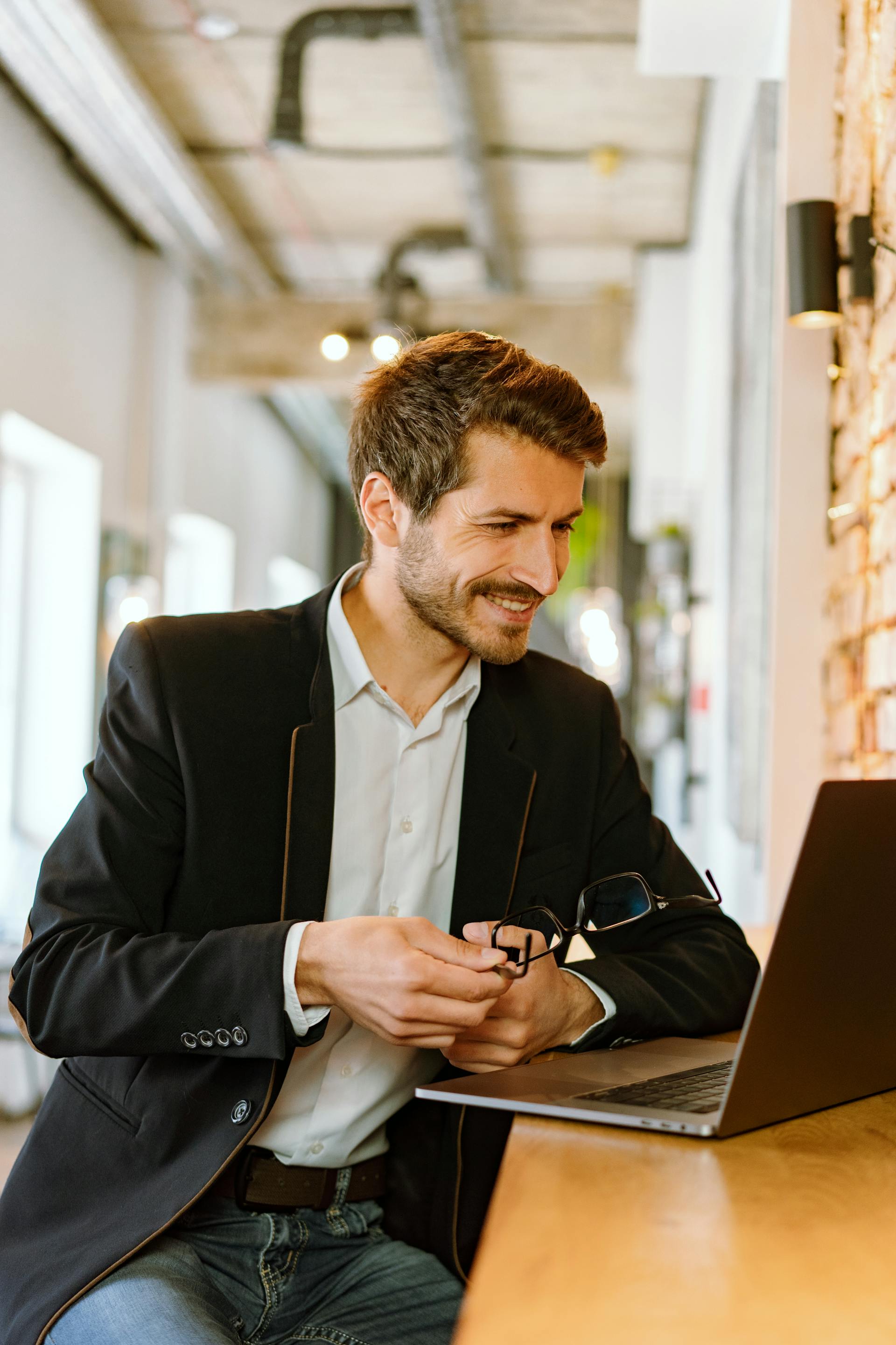 A man in a suit smiles while looking at his laptop | Source: Pexels