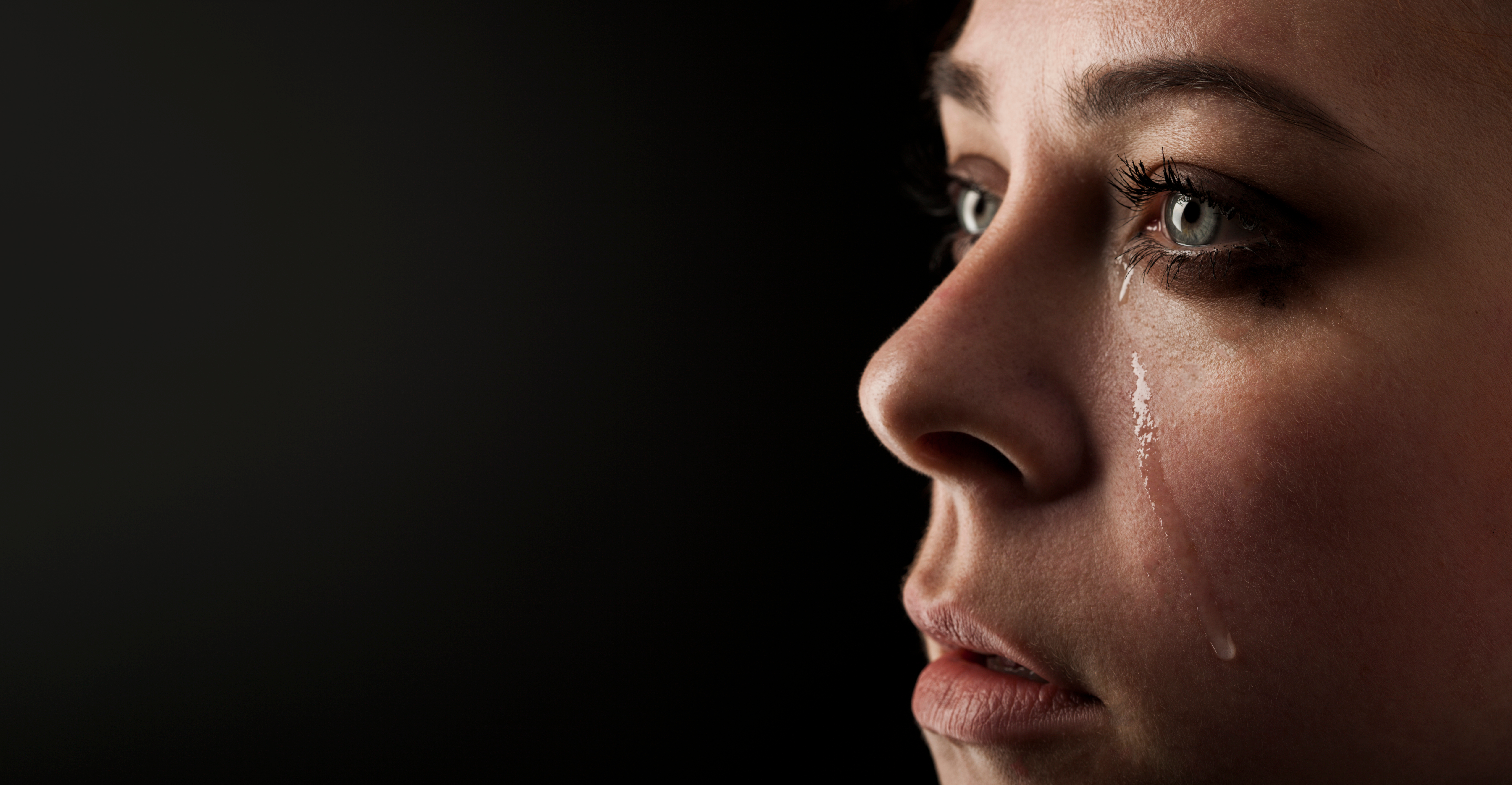 Beautiful girl cries on black background. | Source: Shutterstock