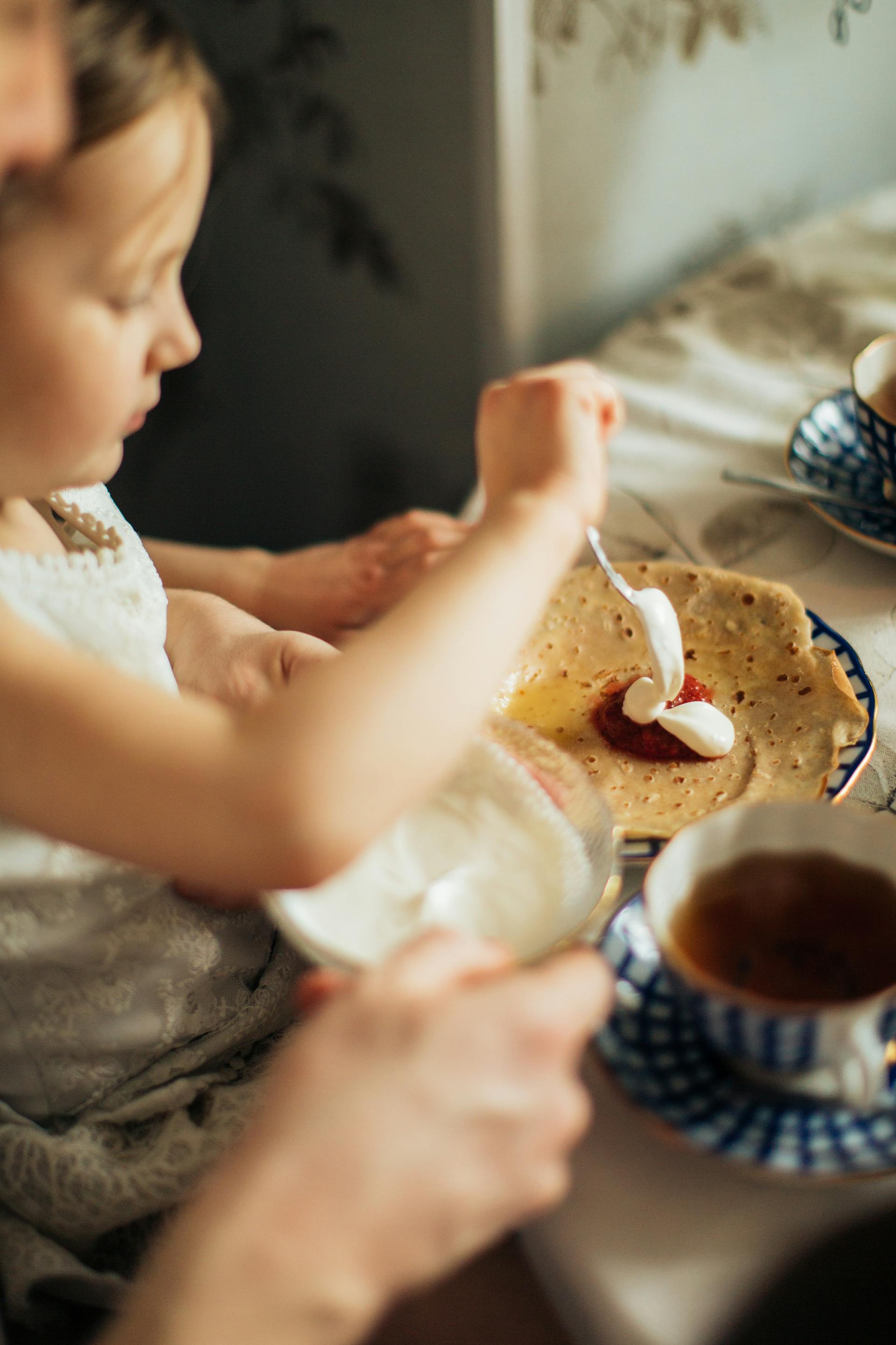 A young girl spreading jam and cream on crepe | Source: Pexels