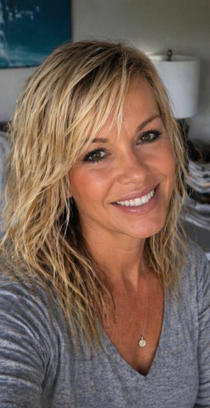 Captured in a more intimate, close-up frame, Katie Piper appears with fuller, shoulder-length waves styled with volume and texture. The darker background draws focus to her bright eyes and wide, confident smile, creating a polished yet approachable portrait that feels both warm and self-assured. | Source: AI