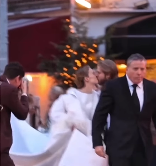 In a blurred, romantic street moment, Maya Hawke and Christian Hutson share a kiss as guests and a photographer surround them. | Source: Instagram/relationships.usa