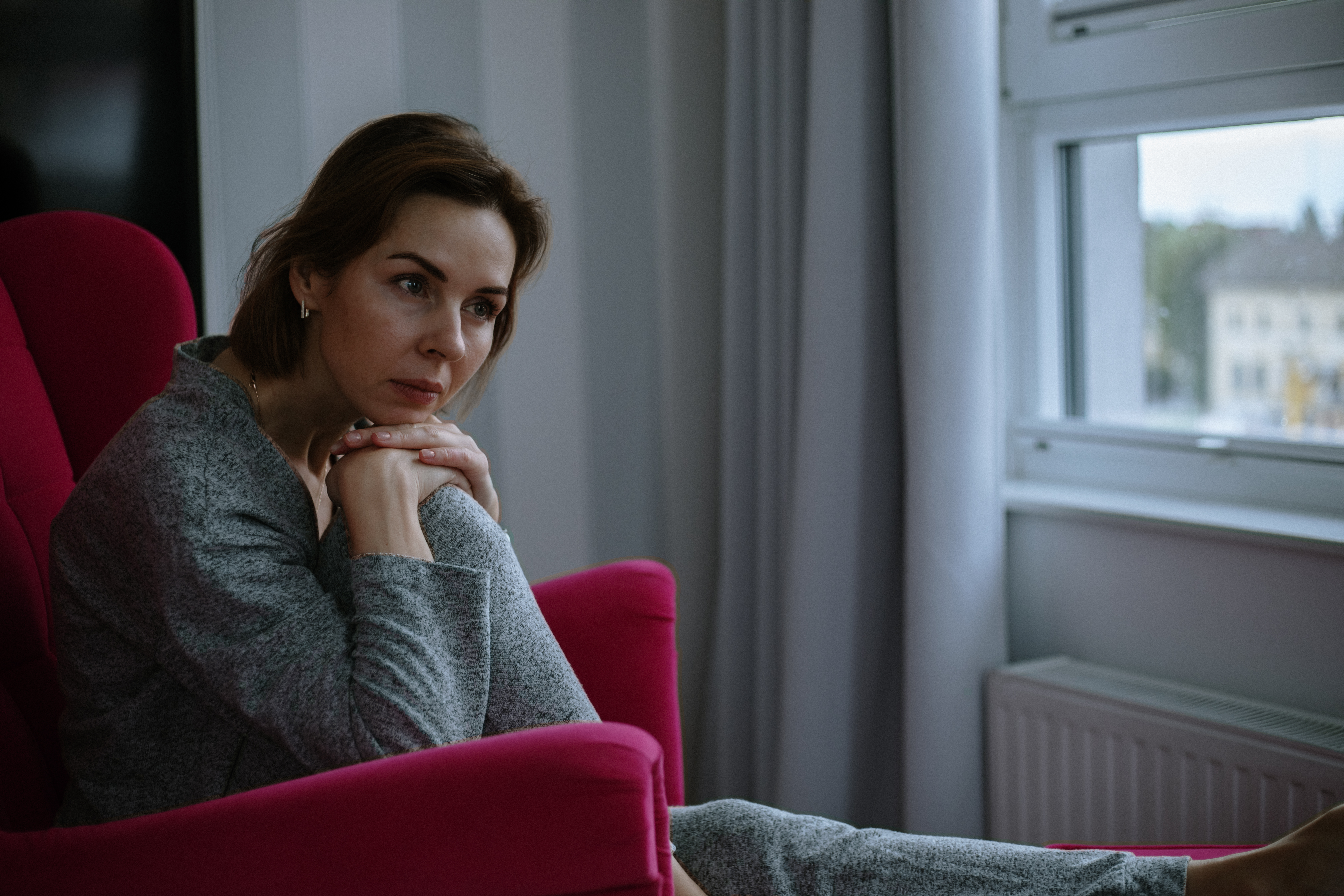 Lounging in comfy red armchair, serene woman in gray home attire sits deep in thought with sense of subdued depression | Source: Getty Images