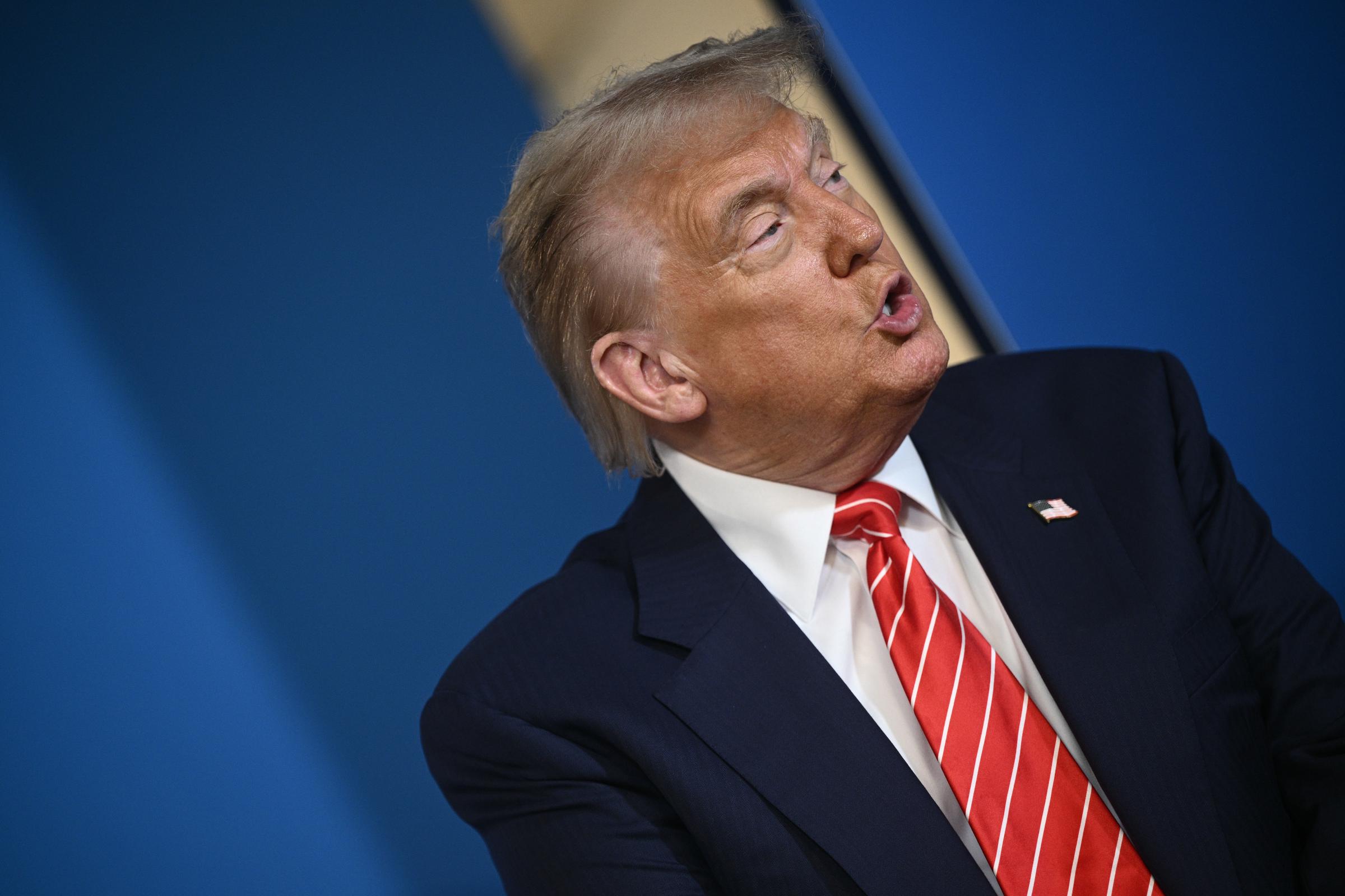 A close-up shot captures Trump mid-speech as he addresses the NATO summit of heads of state and government. His expression is firm and his gaze focused as he puts his points across with measured intensity.