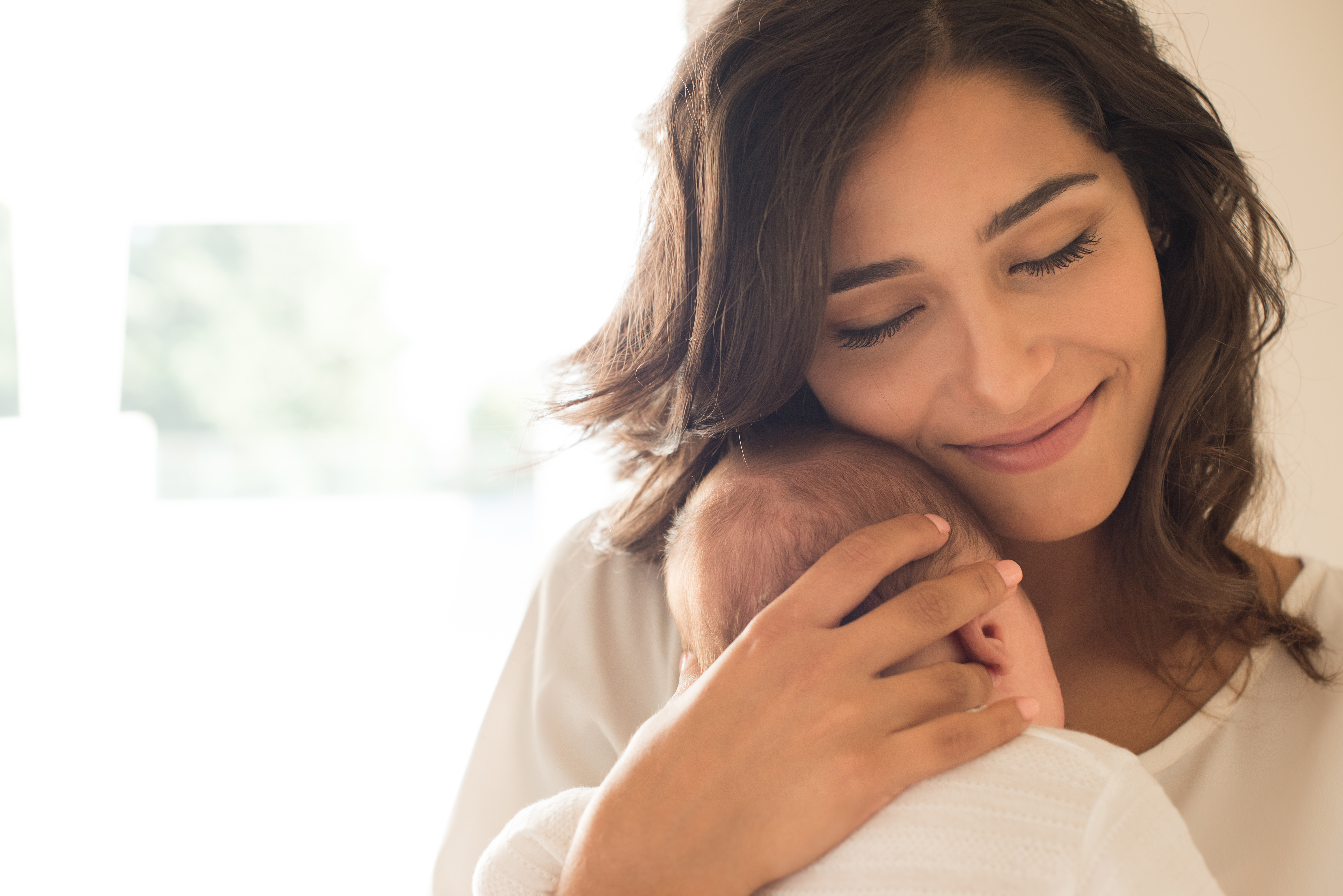 A mother smiling while snuggling her baby to her chest | Source: Shutterstock