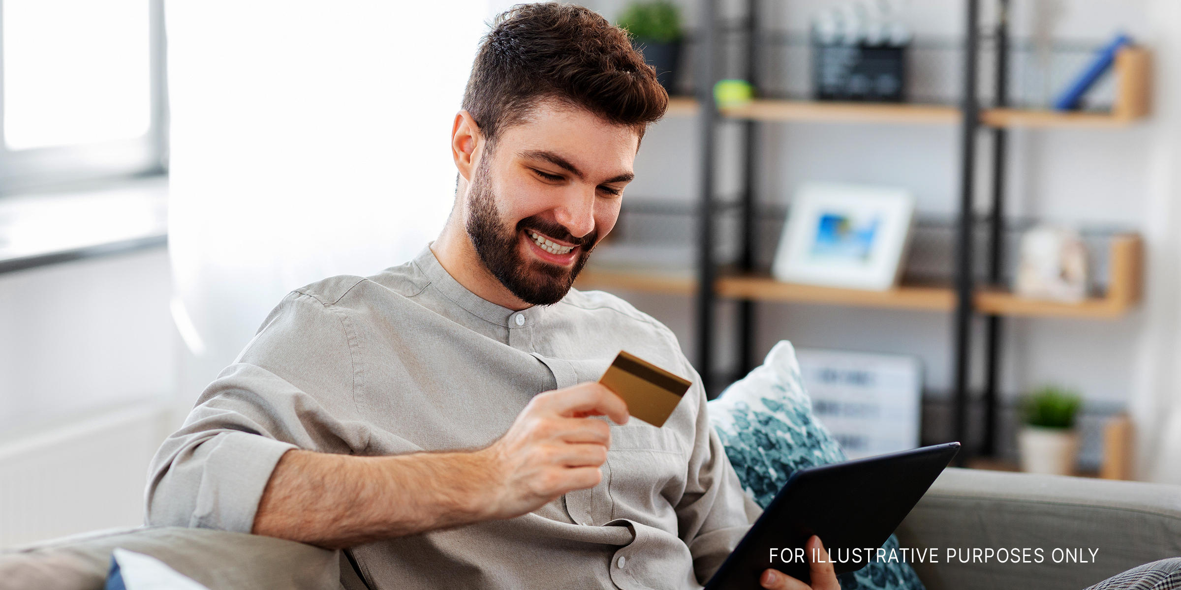 A man smiling while holding a card with a laptop on hand | Source: Shutterstock