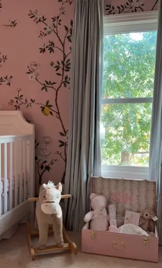 A cozy corner of the nursery showcases a crib alongside a charming rocking horse and a chest filled with soft toys, creating an inviting, storybook atmosphere for baby Sofia. The soft light and floral accents complete this whimsical space. | Source: Instagram/alexmariedrum