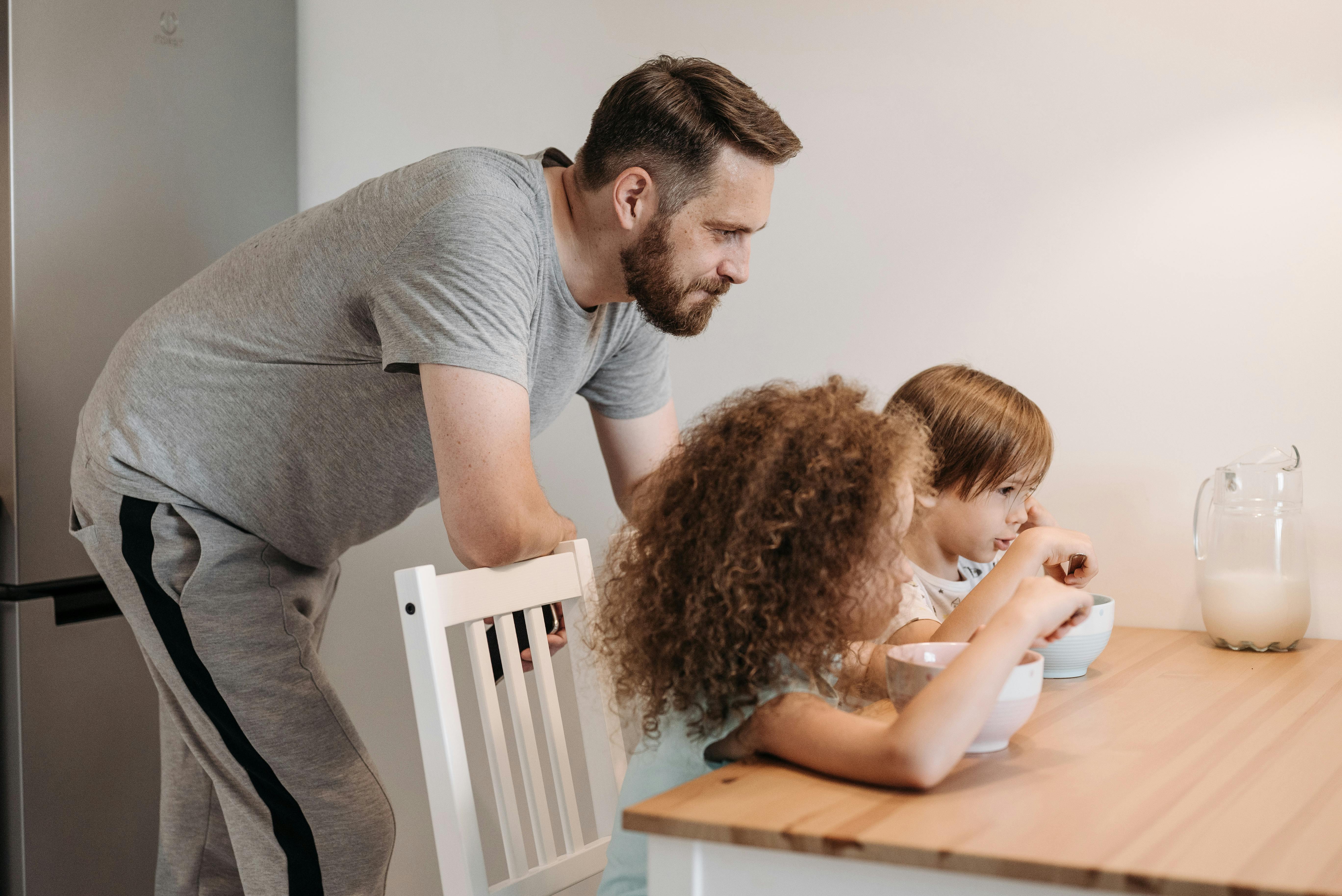 A father watching his two girls eat breakfast | Source: Pexels