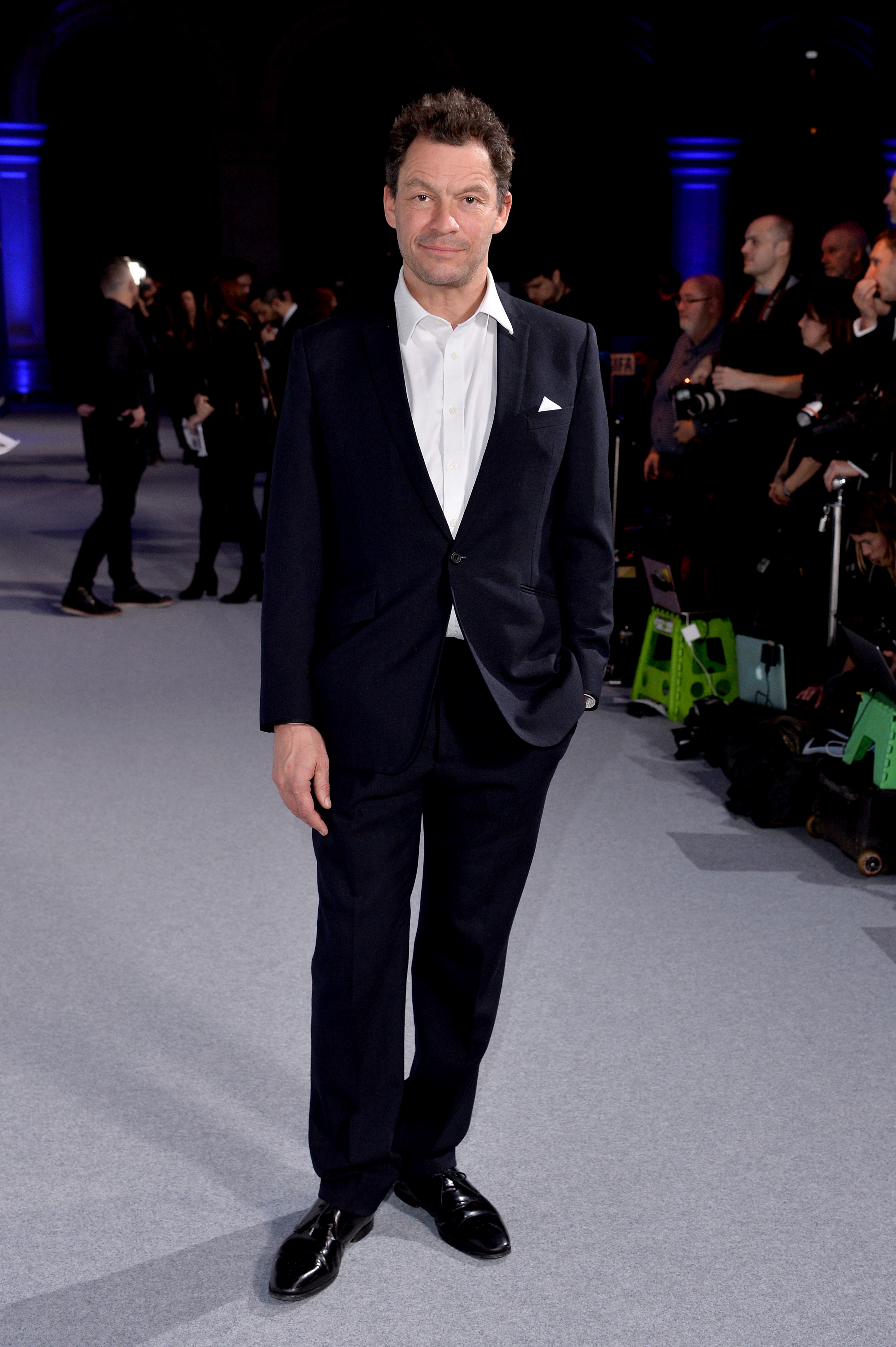 Dominic West attended the 2019 British Independent Film Awards in a classic navy suit paired with a crisp white shirt and no tie. With his hands casually in his pockets and a relaxed smile, he exuded the charm and confidence of a seasoned performer at ease on the red carpet.