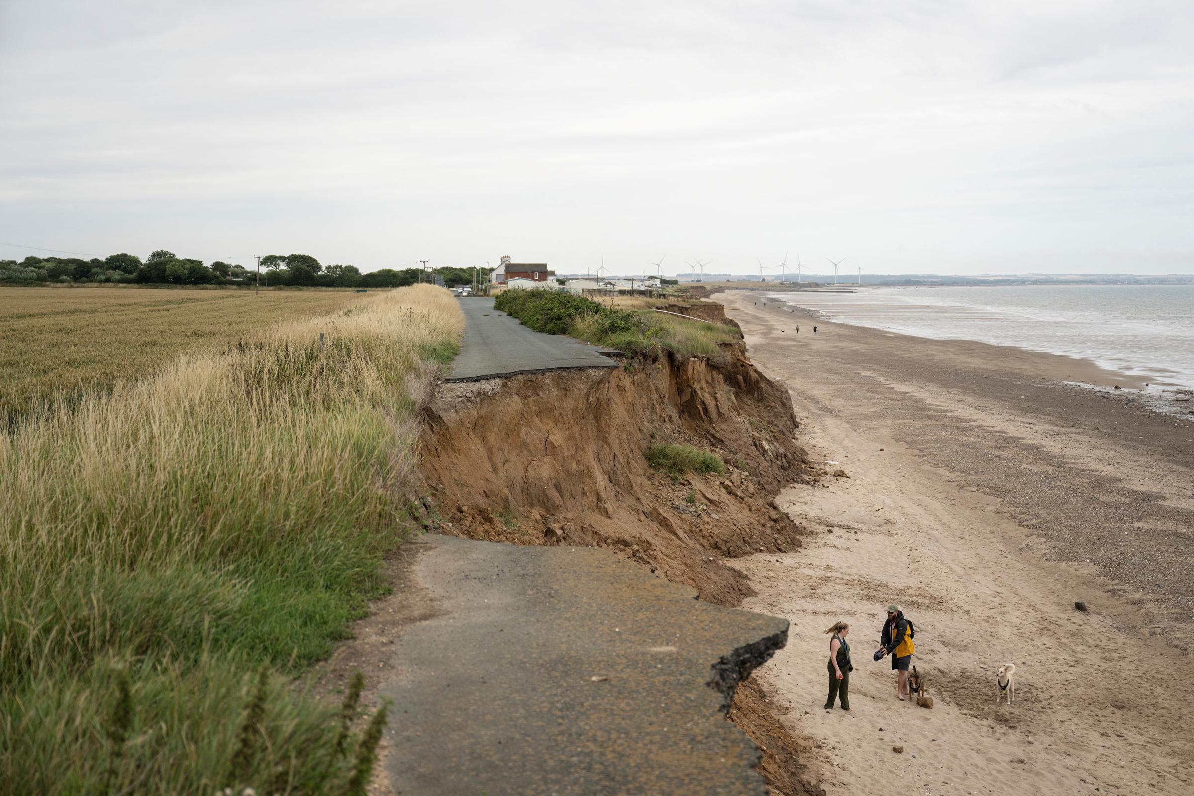 A couple on the beach with their dogs beneath a collapsed road on the North Sea coast undergoing coastal erosion near Bridlington in the East Riding of Yorkshire, England, on July 17, 2025. | Source: Getty Images