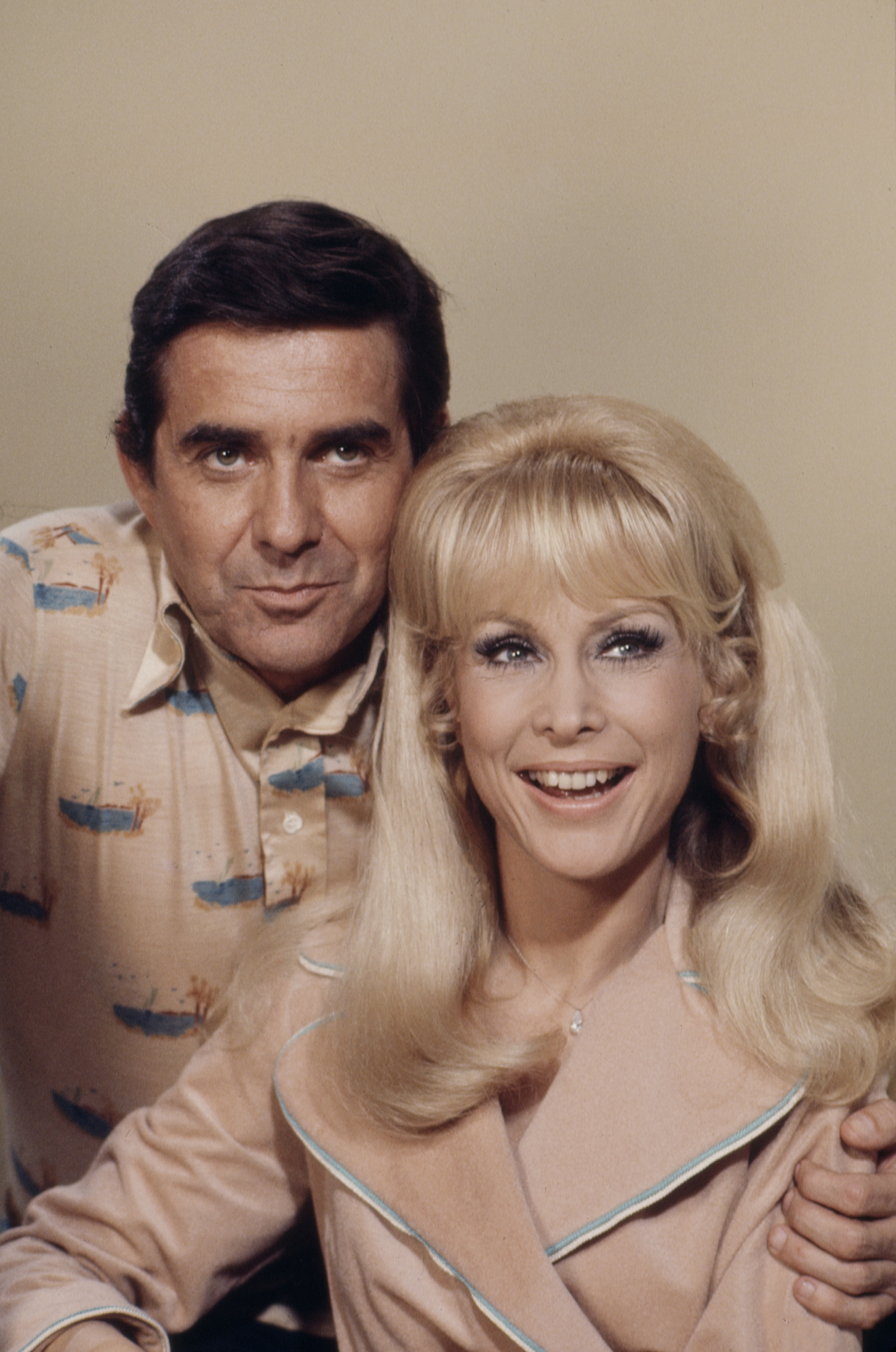 Barbara Eden smiles beside Pat Harrington Jr. in a cheerful promotional portrait for the ABC TV movie "Let’s Switch!" wearing a soft pink outfit and voluminous blond hair.