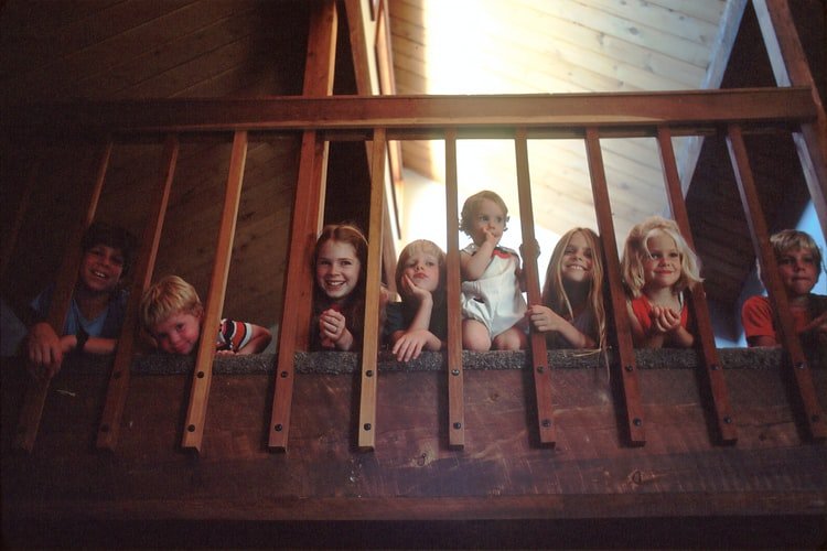 A photo of a large family with seven children peeking through a bannister railing on a staircase. | Photo: Unsplash.