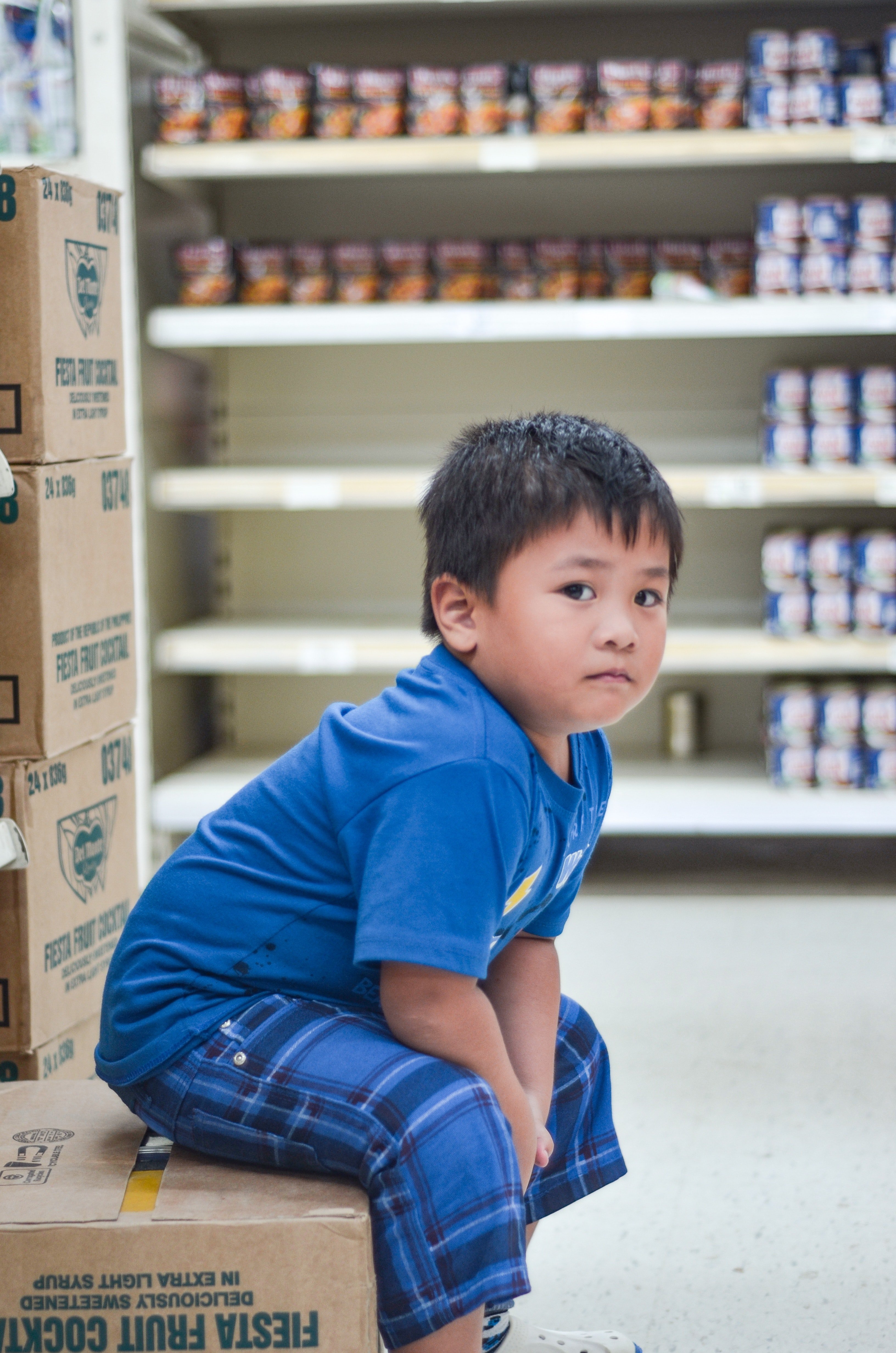 A young boy sitting on a cardboard box in a supermarket | Photo: Pexels