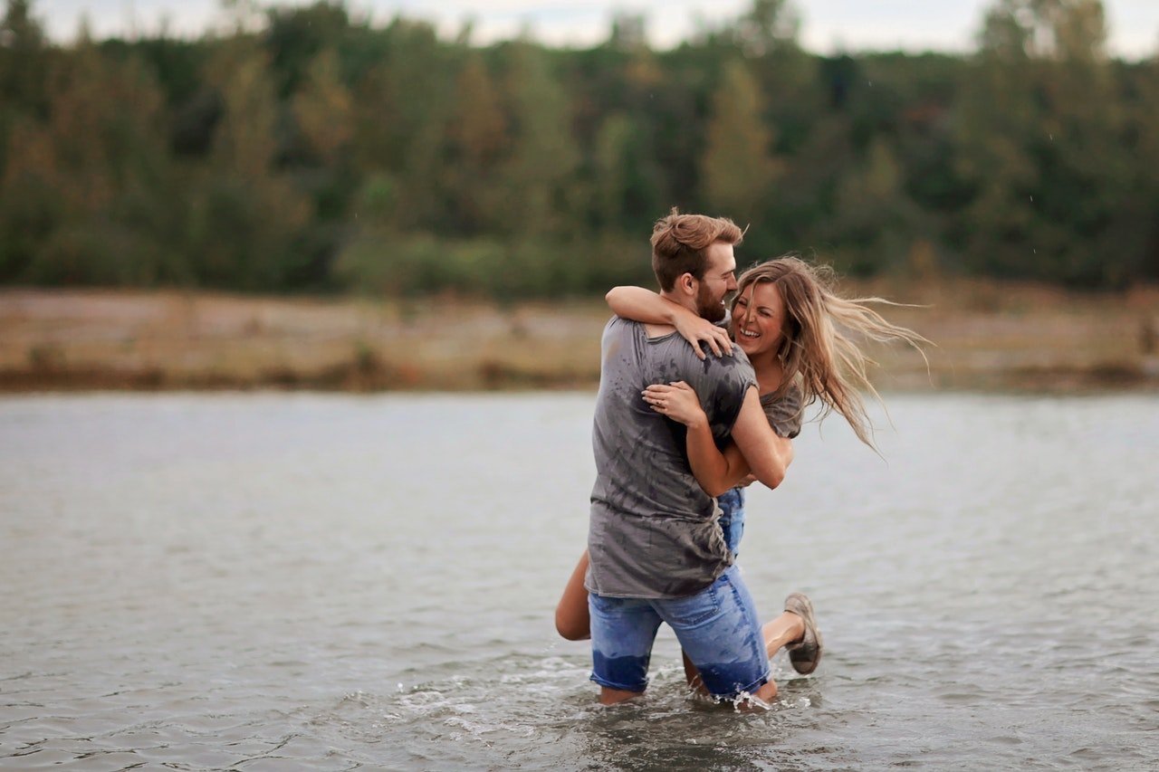 Photo of a man carrying a laughing woman in a lake. | Source: Pexels/LeahKelley