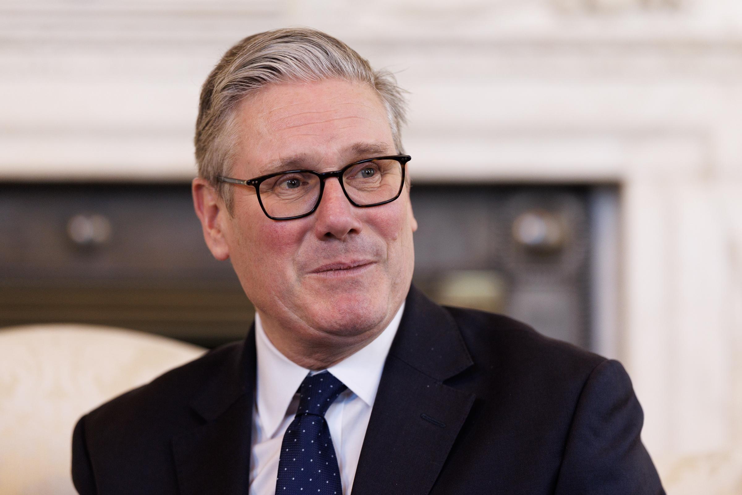 Prime Minister Keir Starmer, dressed in a dark suit and navy dotted tie, listens attentively with a warm, slightly emotional expression during his meeting with Tony and his mother Paula at 10 Downing Street on 17 March 2026. An ornate white fireplace is visible behind him.