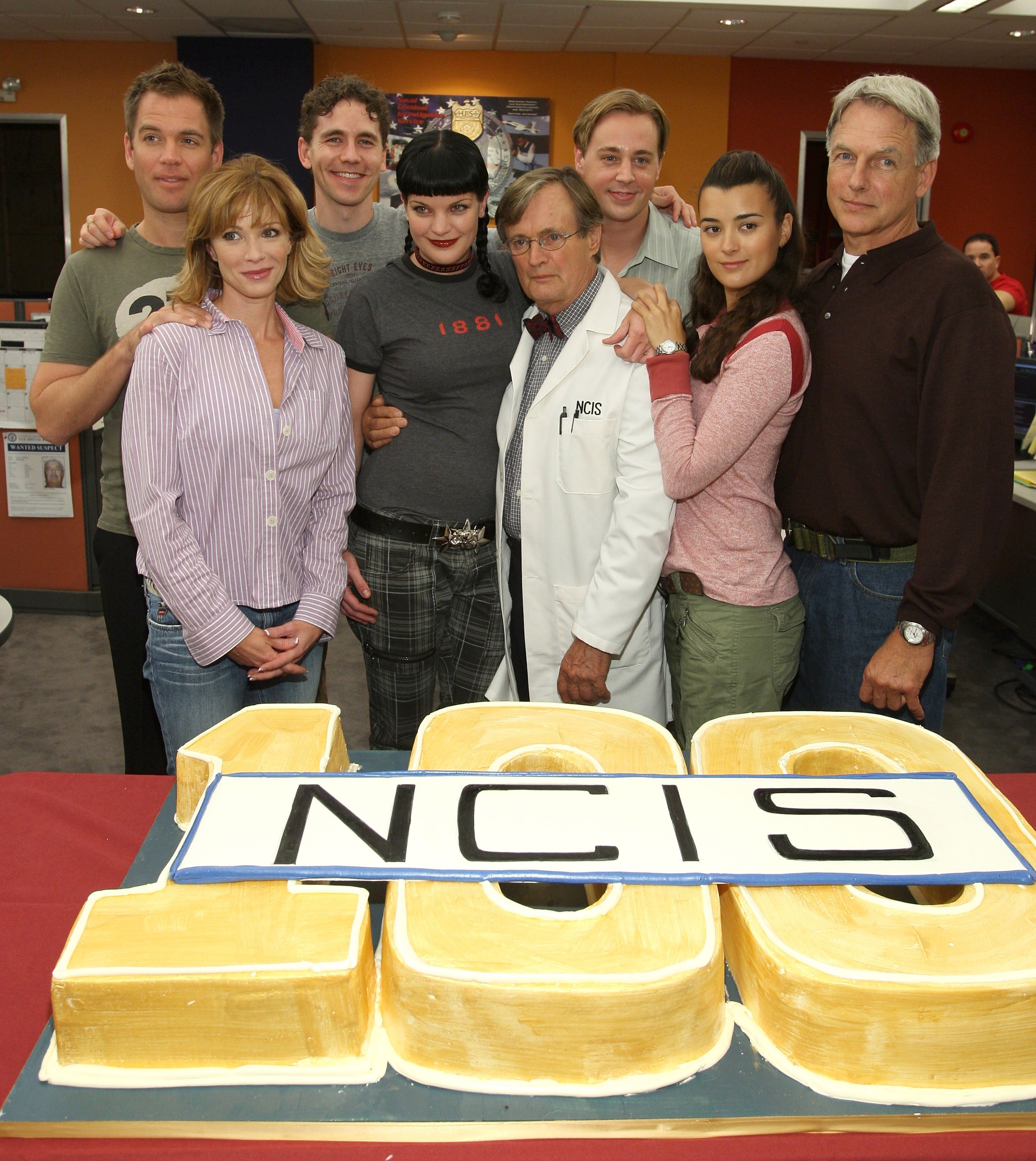 The cast of "NCIS" celebrating 100 episodes of the show with a large cake. 2007, California. | Photo: Getty Images
