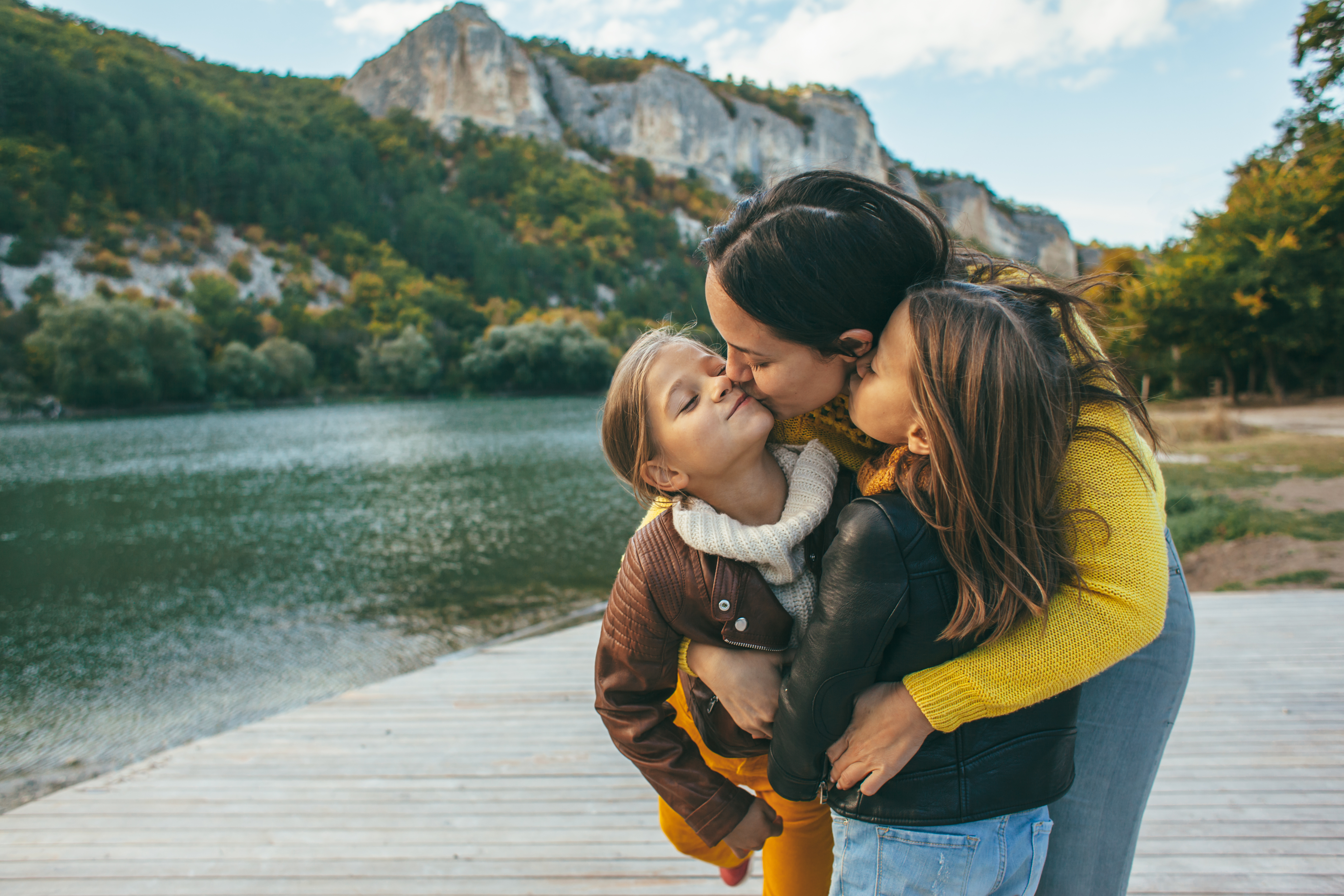 A woman kisses her little girls standing near a pond | Source: Shutterstock
