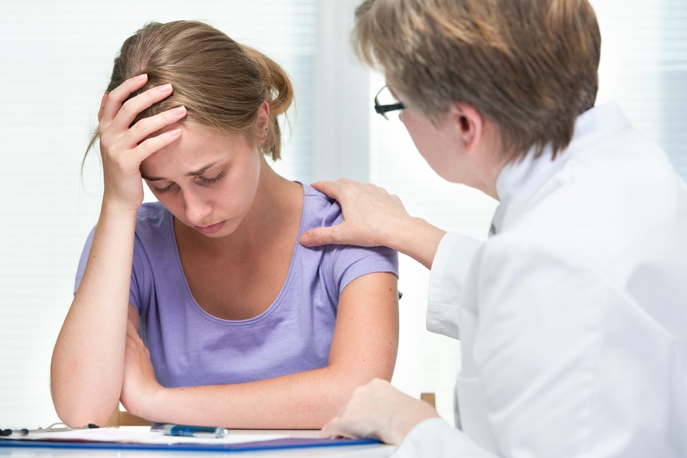 Mujer angustiada sosteniendo su cabeza con su mano mientras consulta a una doctora. | Foto: Shutterstock