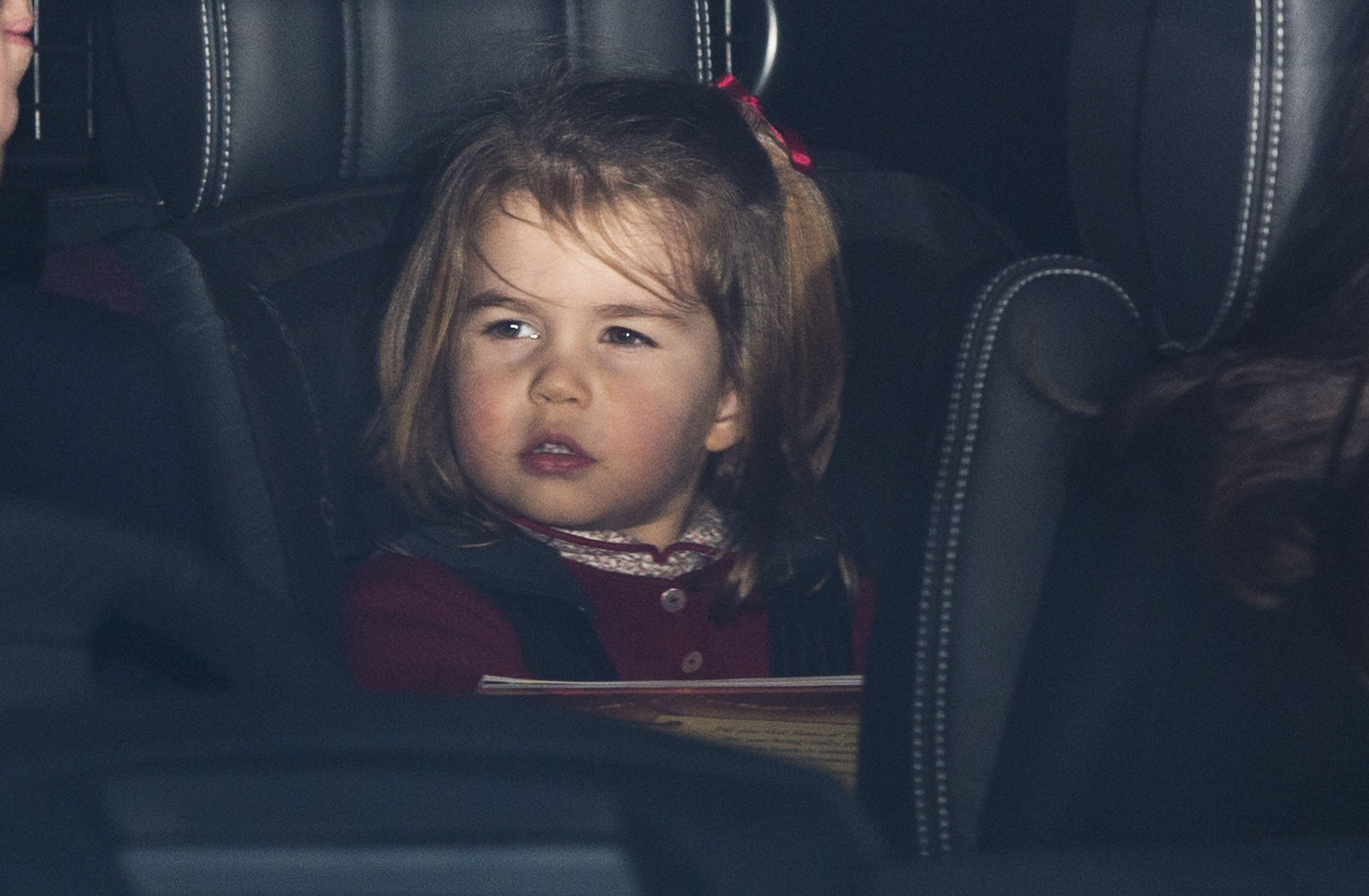 Two-year-old Charlotte peers solemnly through a car window, red bow in her hair, as she arrives at Buckingham Palace for the royal family's Christmas lunch in December 2017.