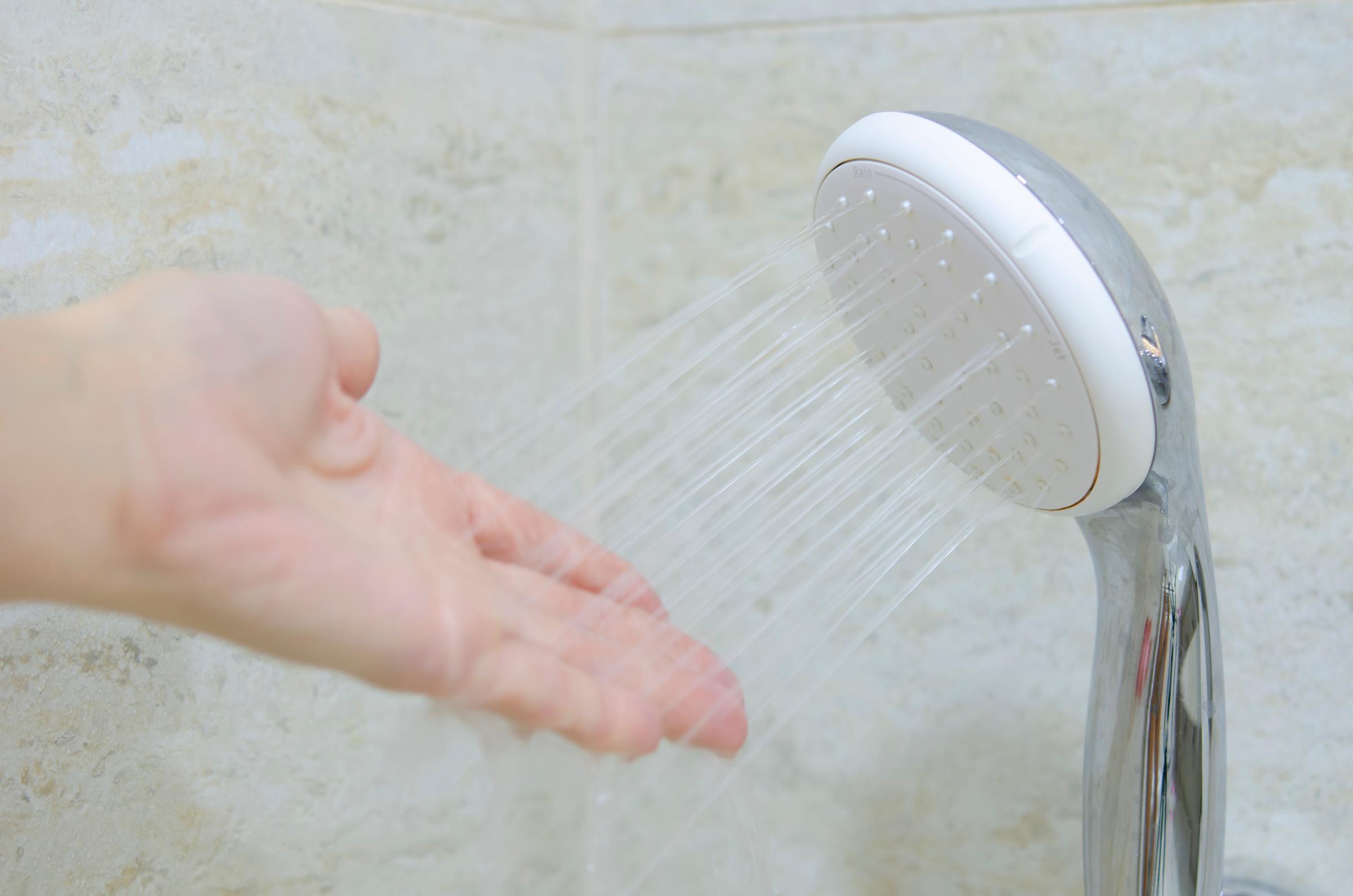 A hand feeling the water coming out of a shower spout | Source: Shutterstock